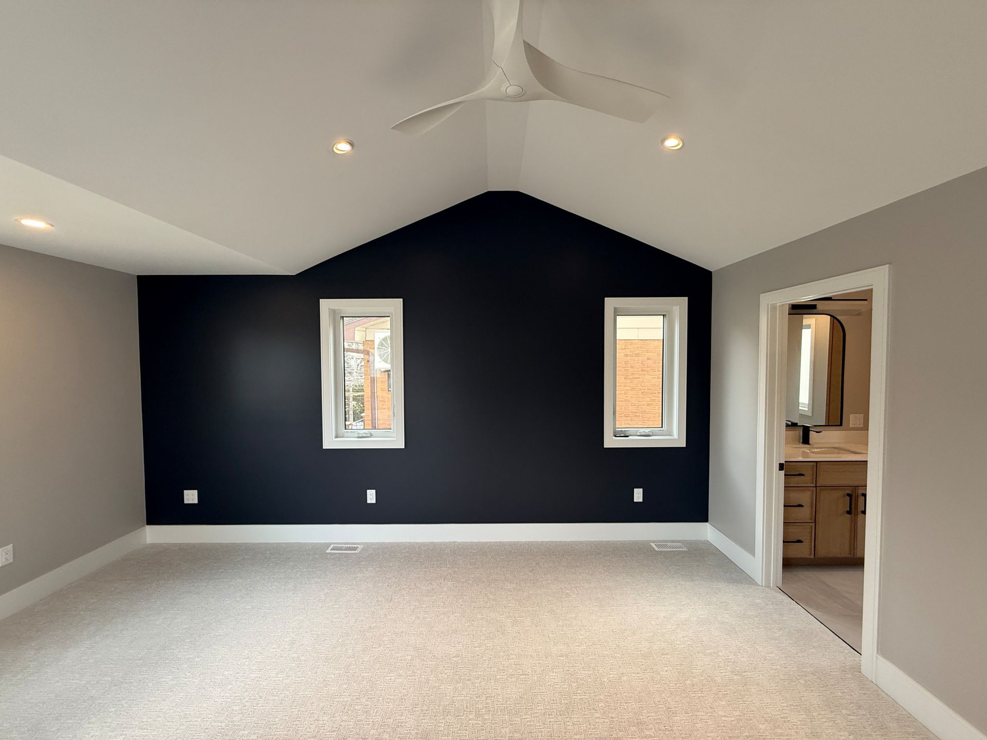 Empty bedroom with gray walls, a black accent wall, two windows, and a ceiling fan.