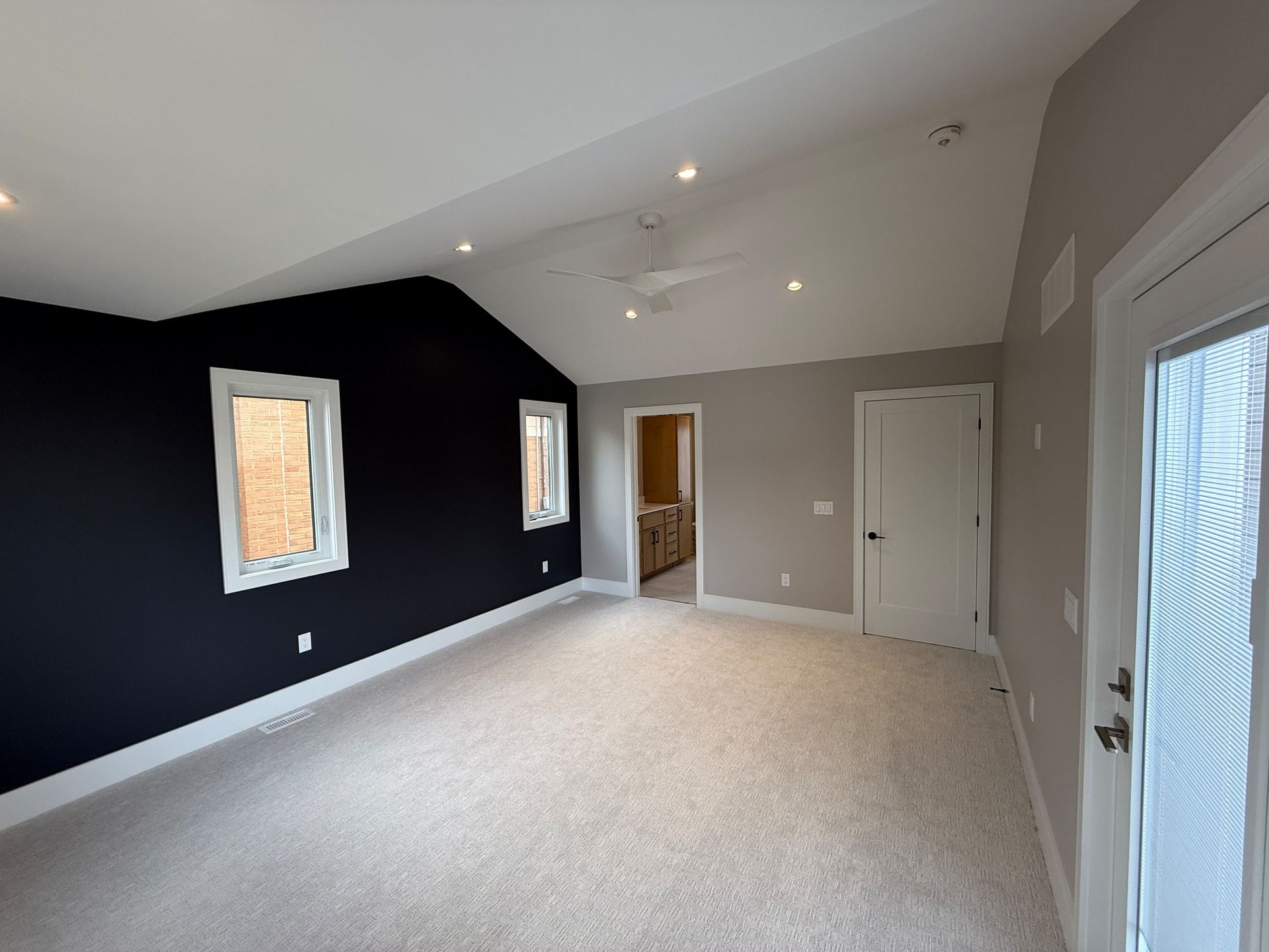 Bedroom with black accent wall, white ceiling, and beige carpet. Two windows, a door, and recessed lighting.