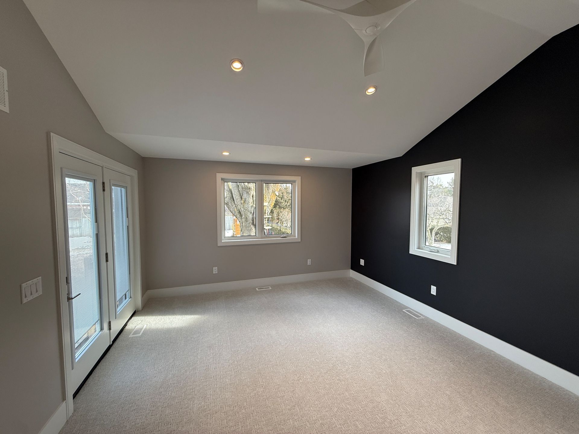 Empty bedroom with light carpet, gray and black walls, and white trim.