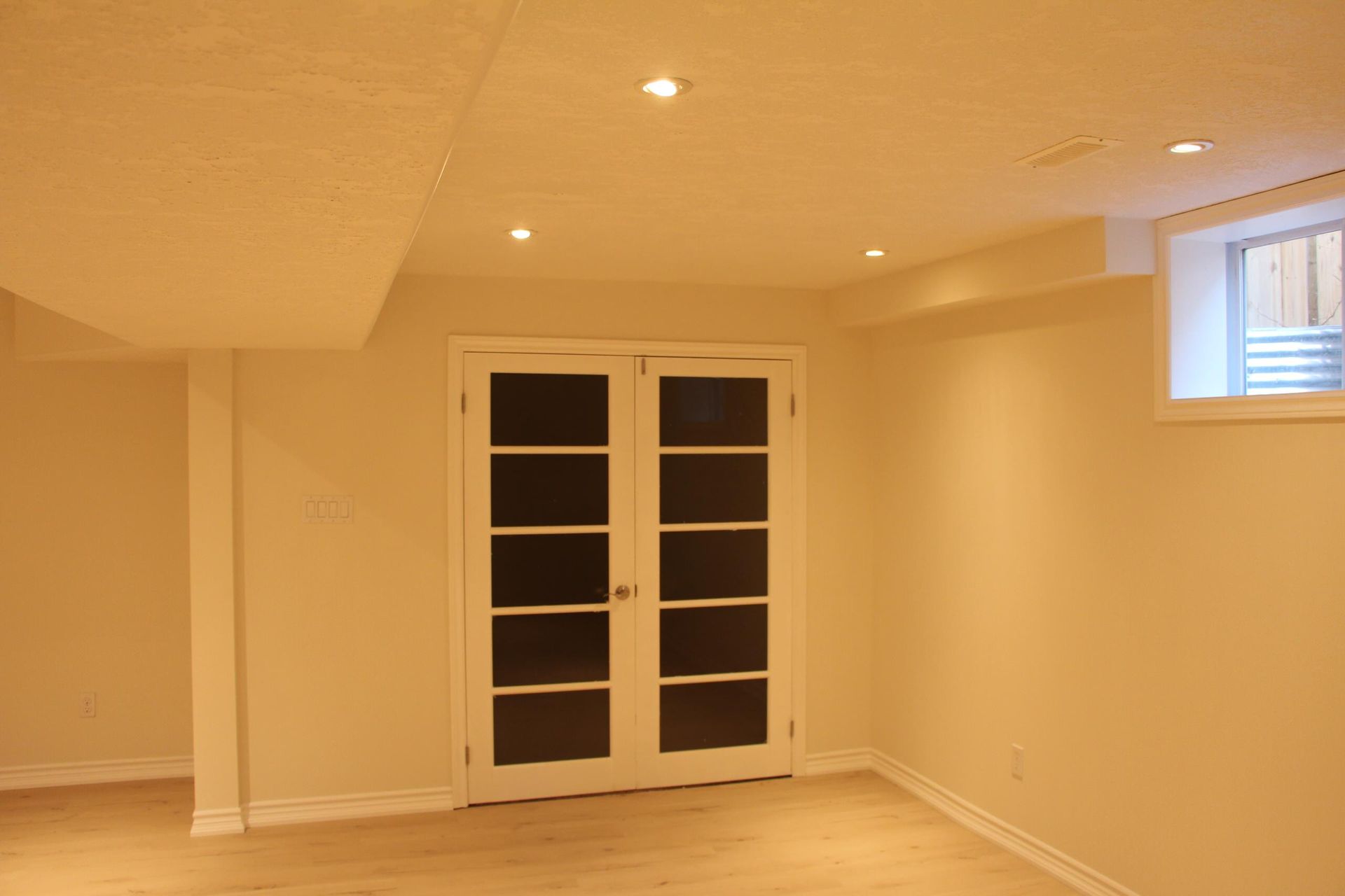Empty room with white walls, wooden floor, recessed lighting, and French doors.