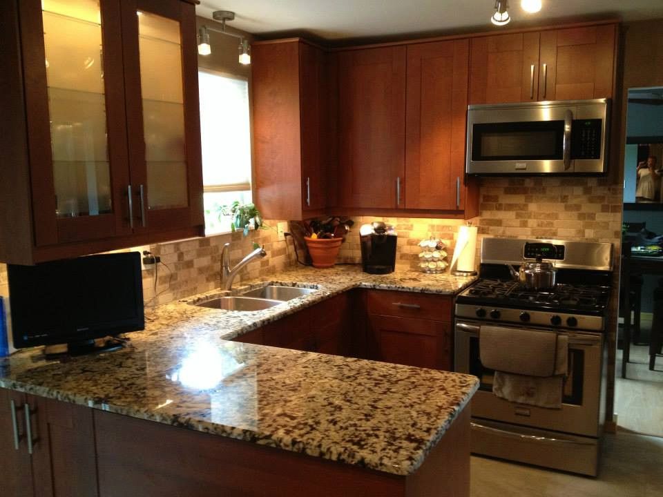 U-shaped kitchen with brown cabinets, granite countertops, stainless steel appliances, and a stone tile backsplash.