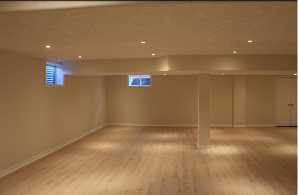 Empty finished basement with wood floor, recessed lighting, and small windows.