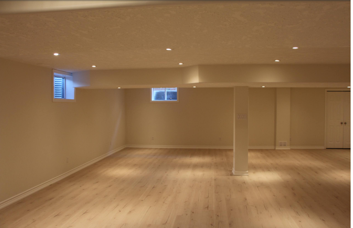 Empty, light-colored basement with wooden floor, recessed lighting, and two small windows.