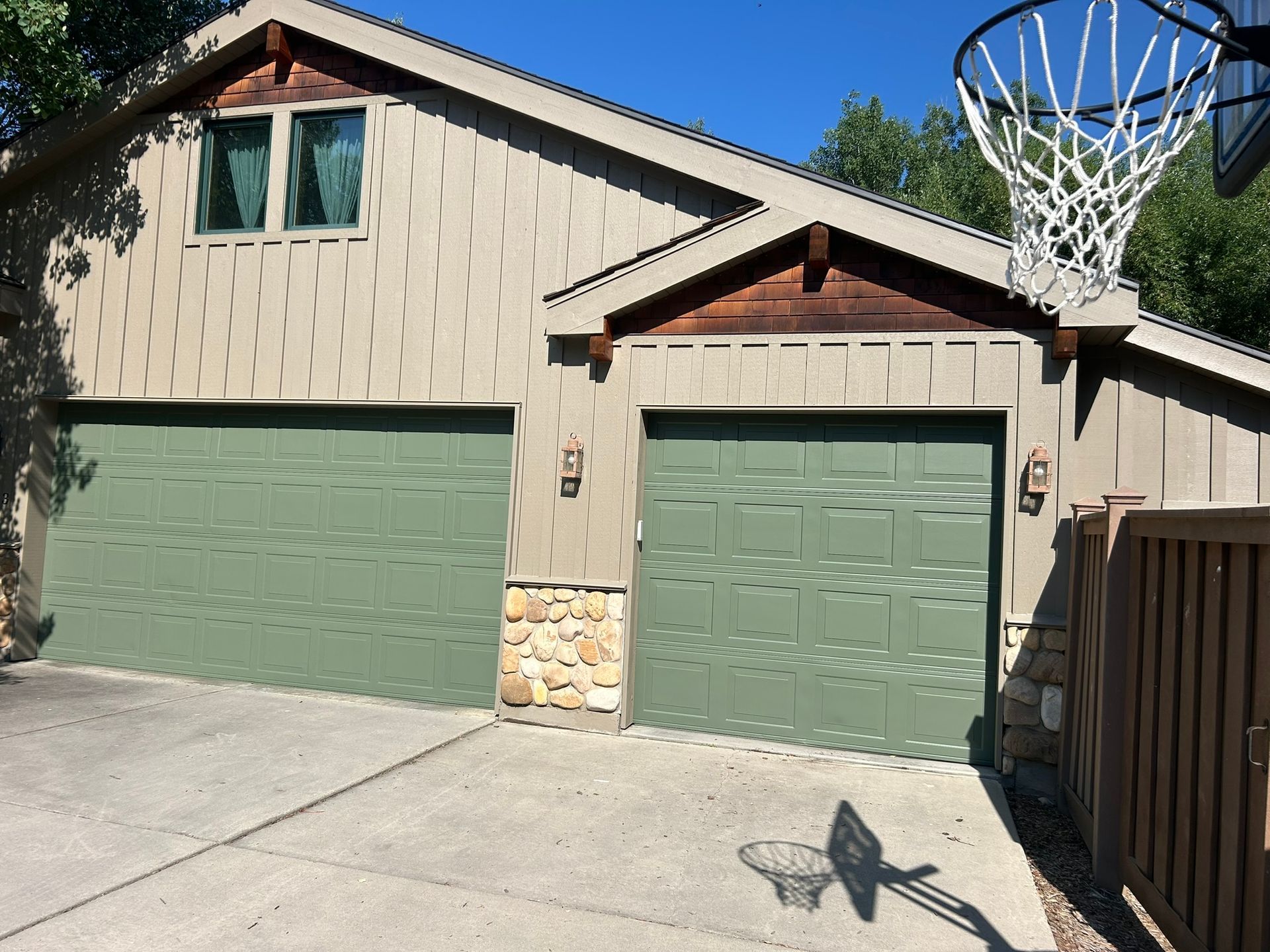 A house with two green garage doors and a basketball hoop in front of it.