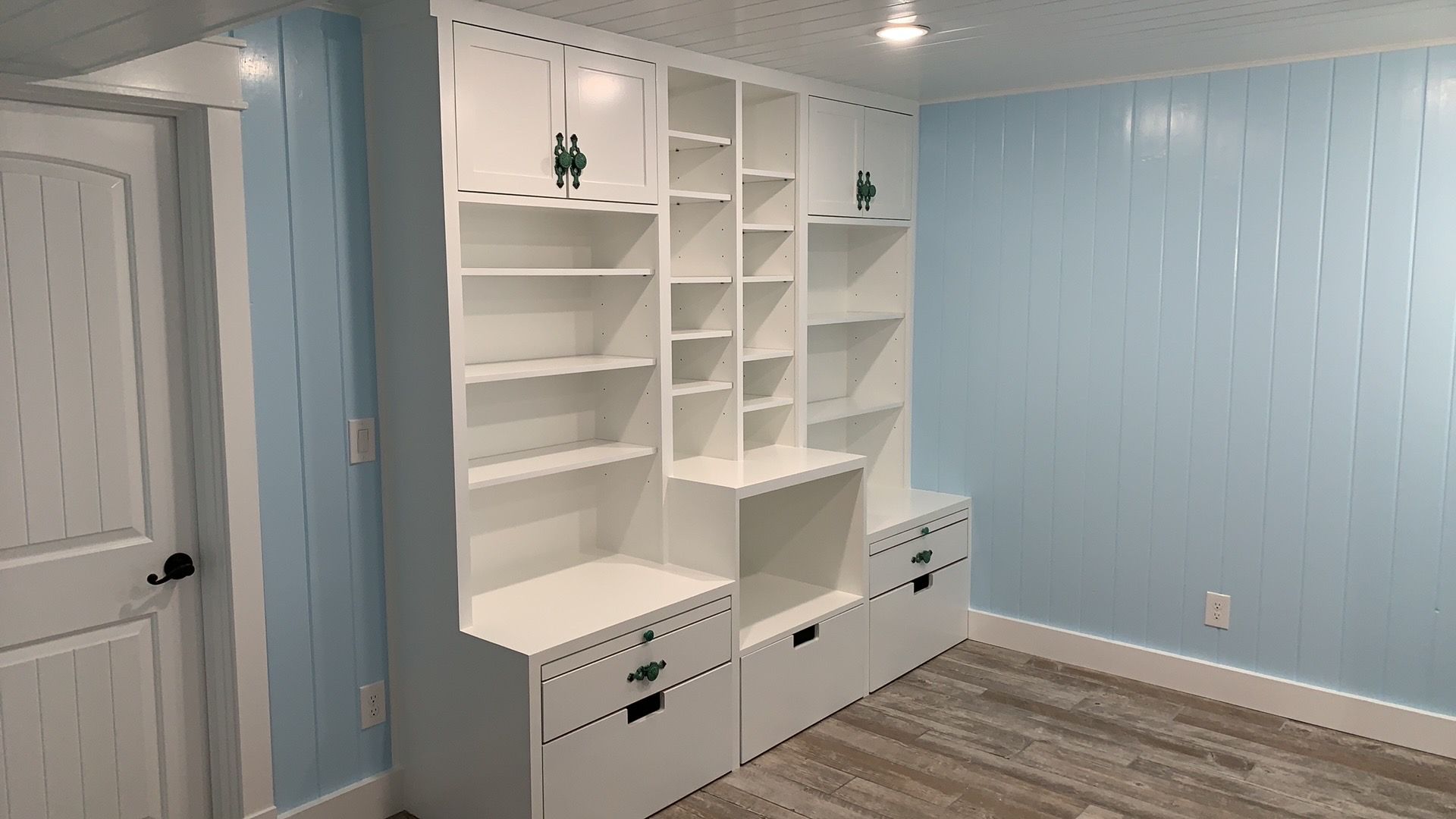 A room with blue walls and white shelves and drawers.