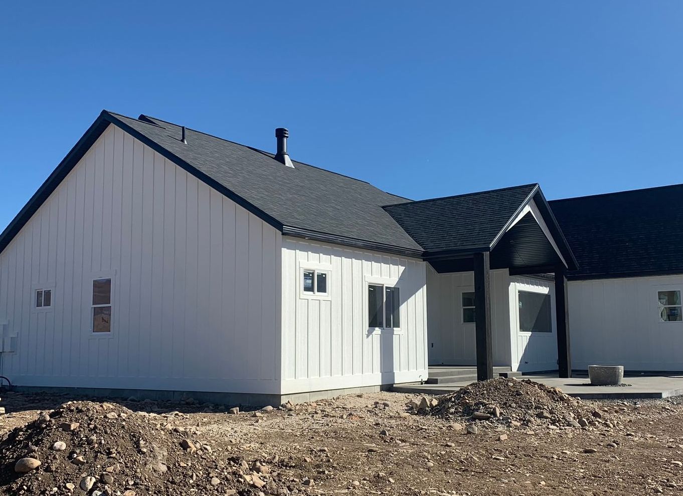 A white house with a black roof is sitting on top of a dirt field.