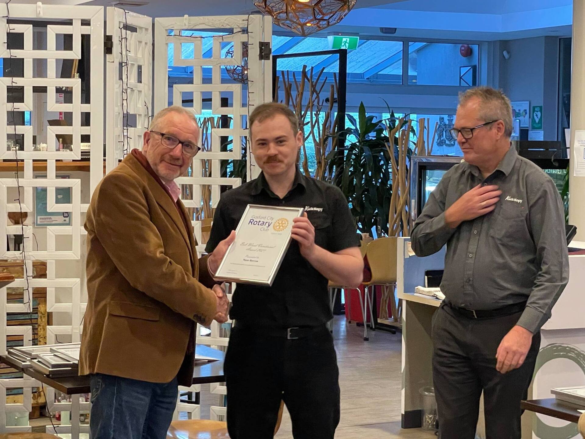 Two men are shaking hands with a man holding a certificate.