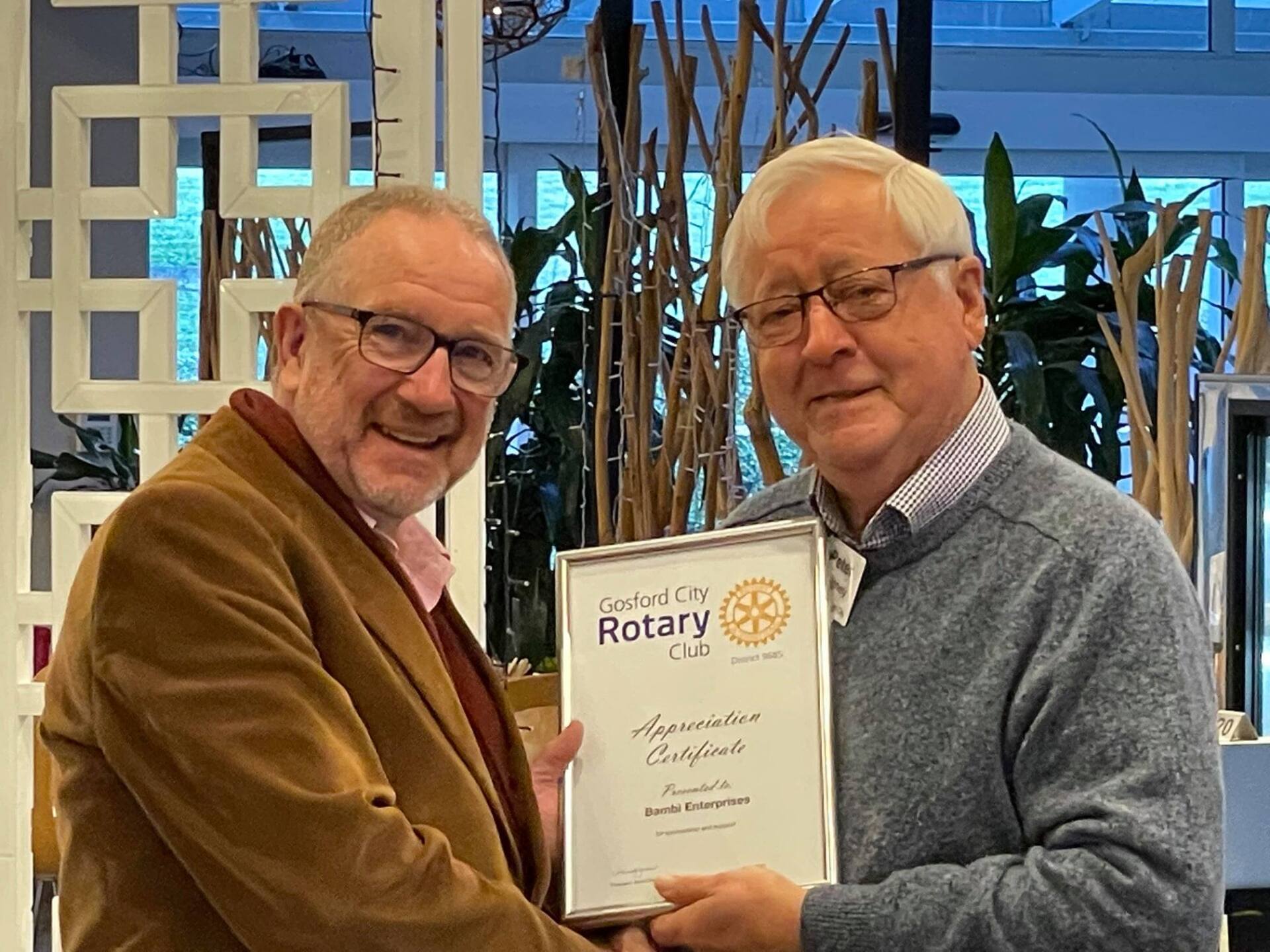 Two men are shaking hands while holding a certificate from the rotary club.