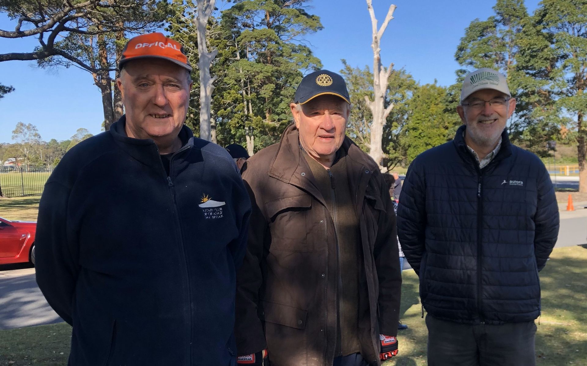 Three men are standing next to each other in a park.