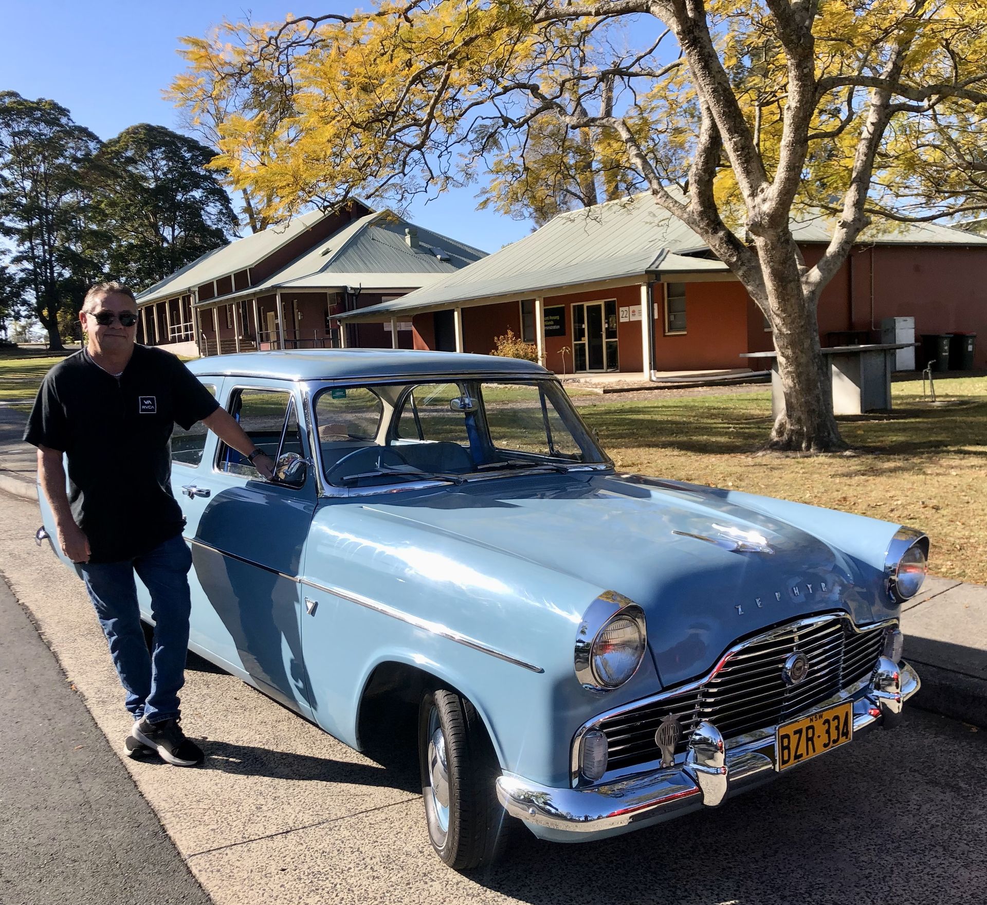 A man is standing next to a blue car with a license plate that says eek 924