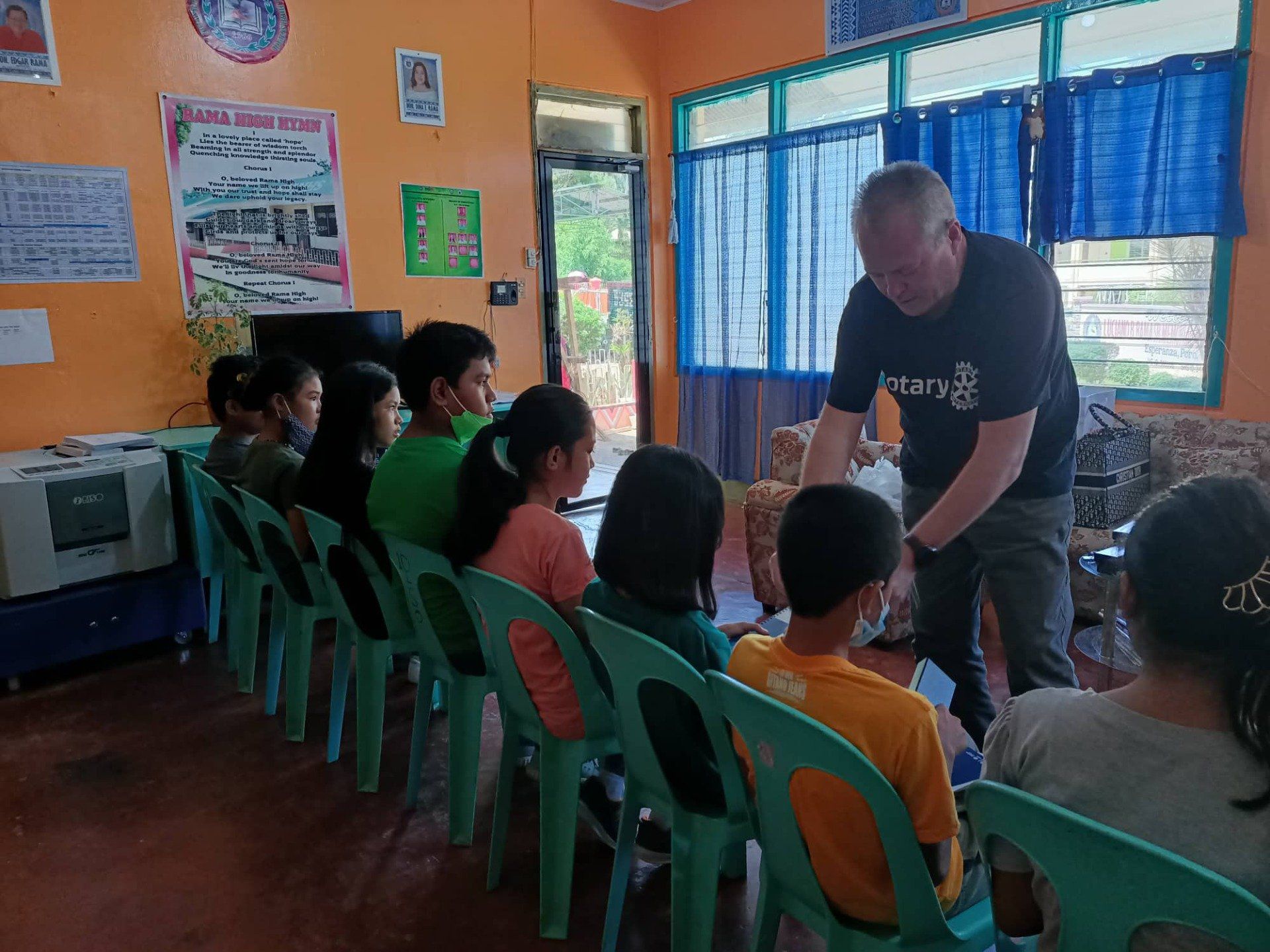 A man is standing in front of a group of children sitting in chairs.