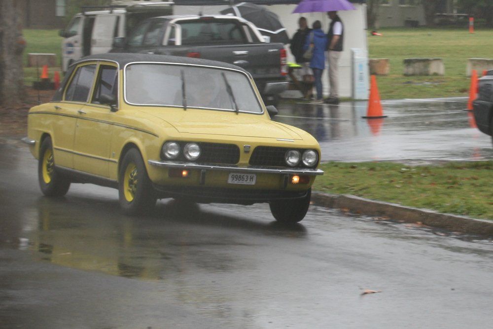 A yellow car is driving down a wet street