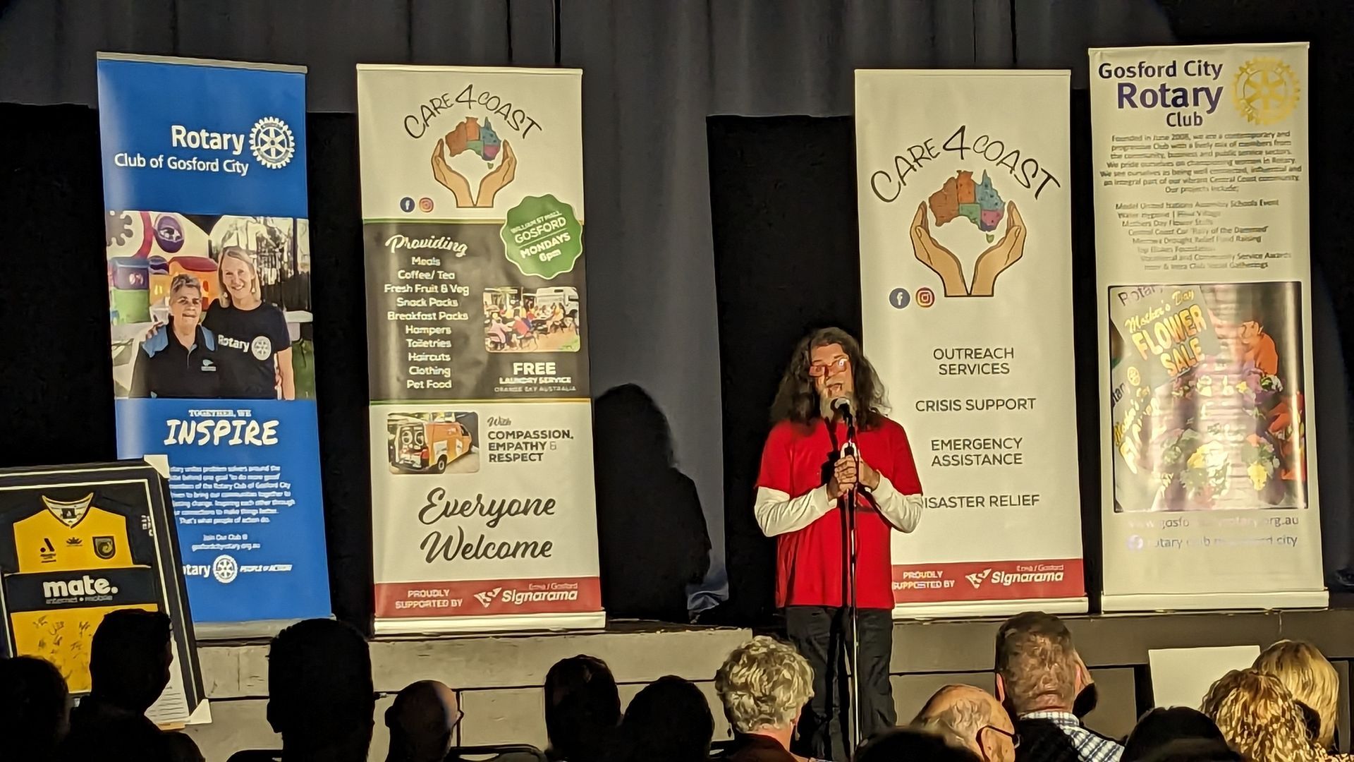 A woman stands in front of a microphone in front of a group of people