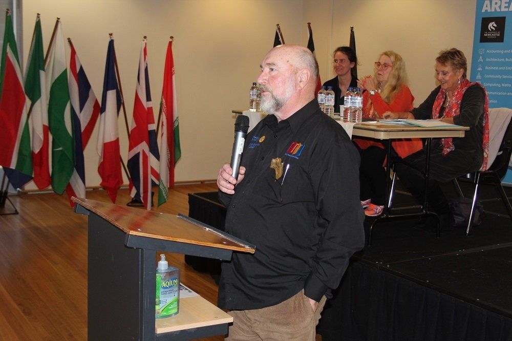 A man stands at a podium holding a microphone in front of a group of people