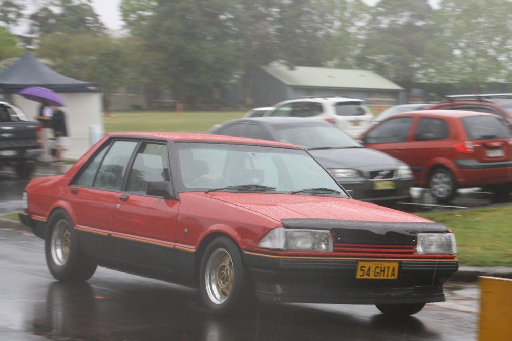 A red car with a license plate that says x4 dna is parked in the rain
