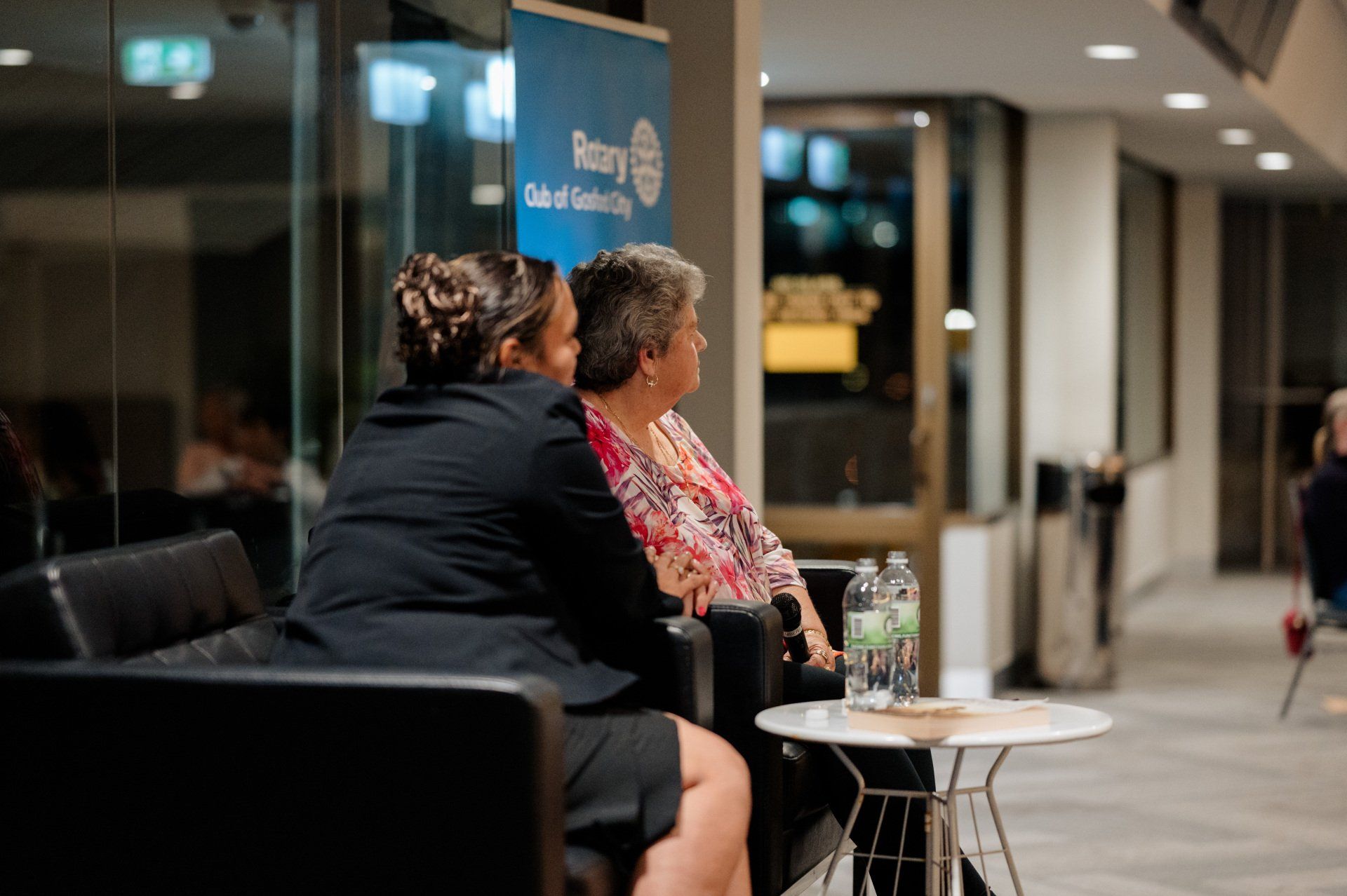 Two women are sitting in chairs talking to each other in a hallway.