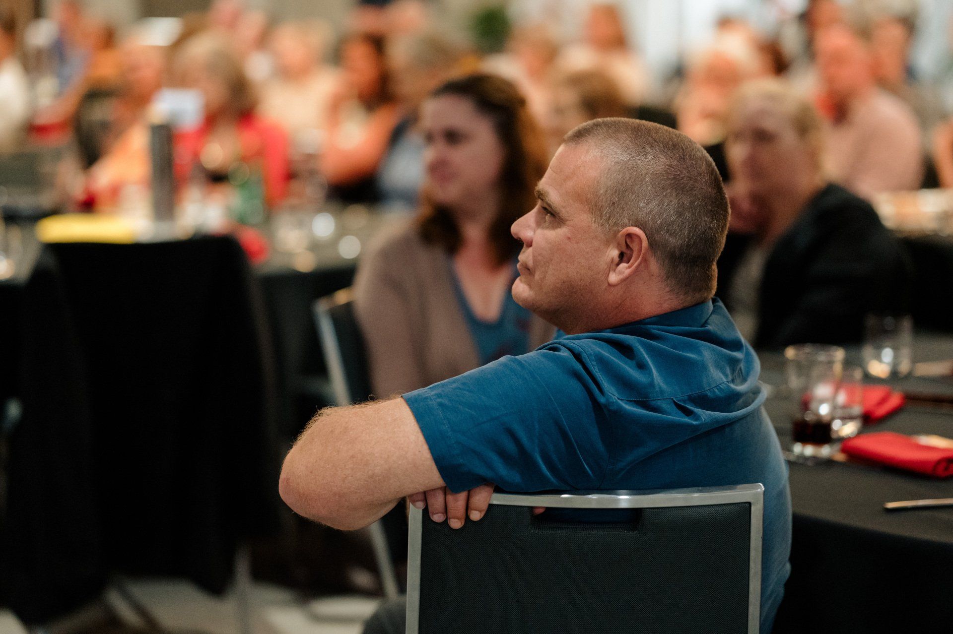 A man in a blue shirt is sitting in a chair at a table.