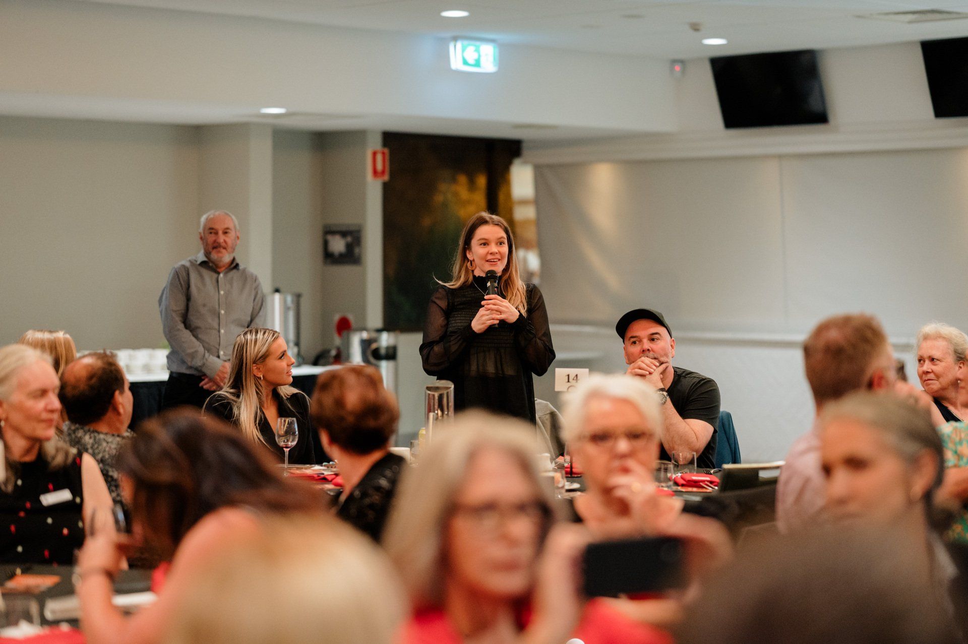 A woman is standing in front of a crowd of people holding a microphone.