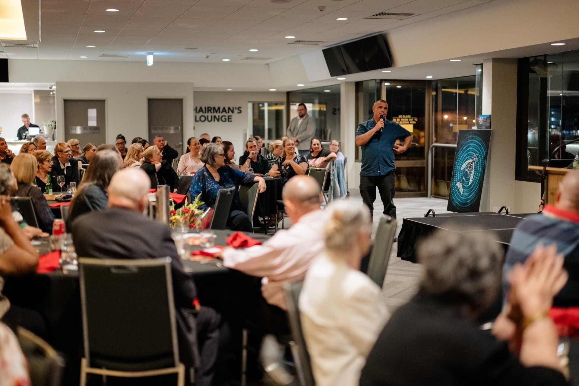 A man is standing in front of a crowd of people at a dinner party.