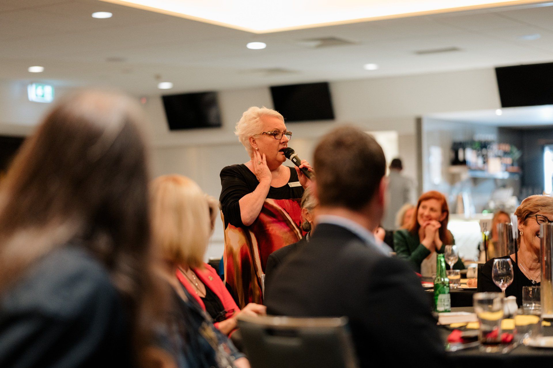 A woman is speaking into a microphone while sitting at a table with other people.