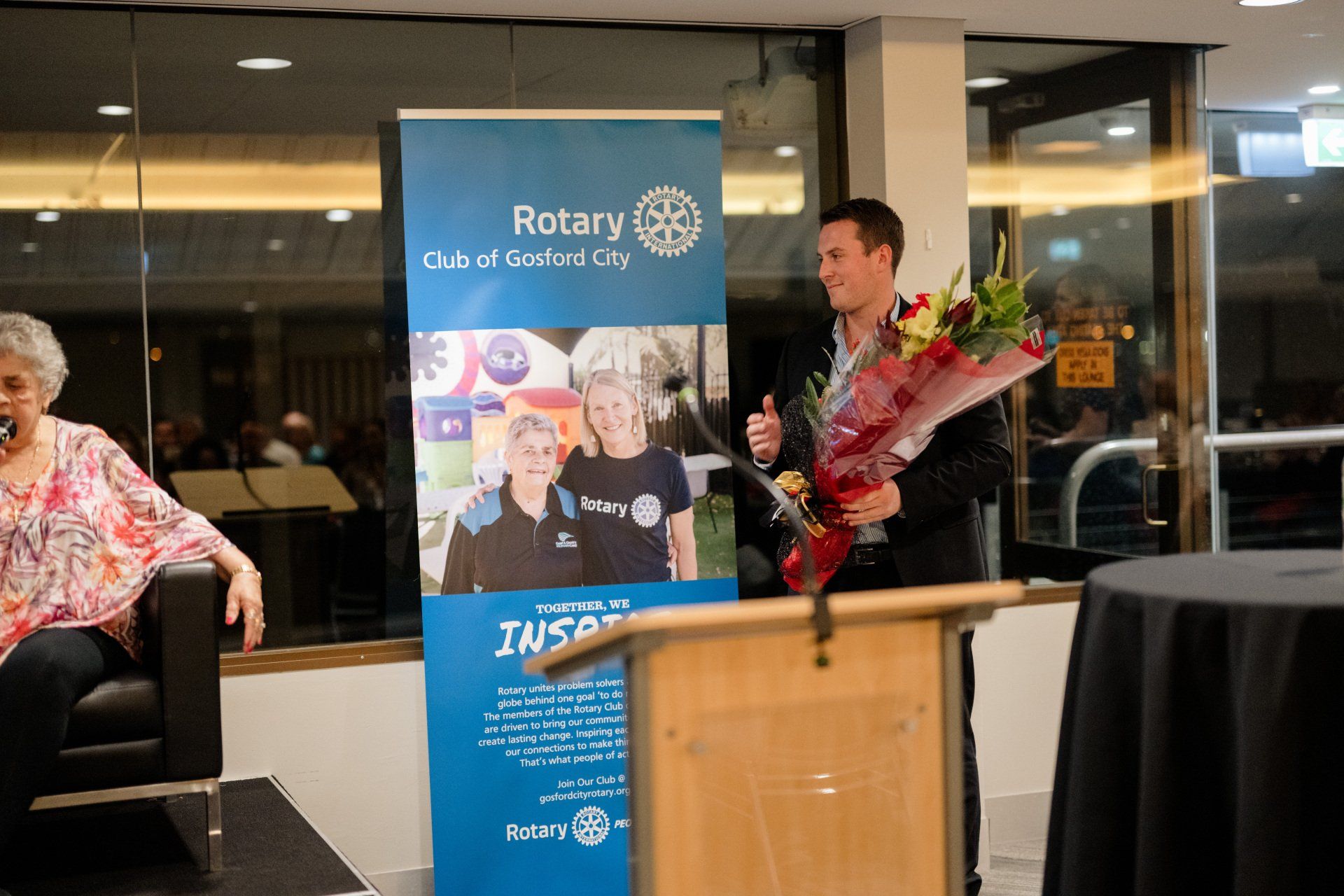A man is holding a bouquet of flowers in front of a rotary sign.