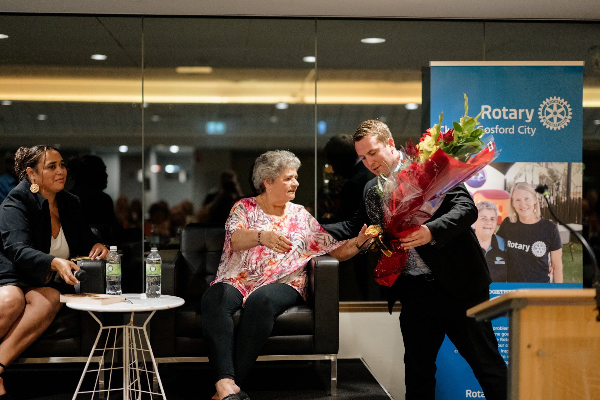 A man is giving a bouquet of flowers to a woman sitting in a chair.
