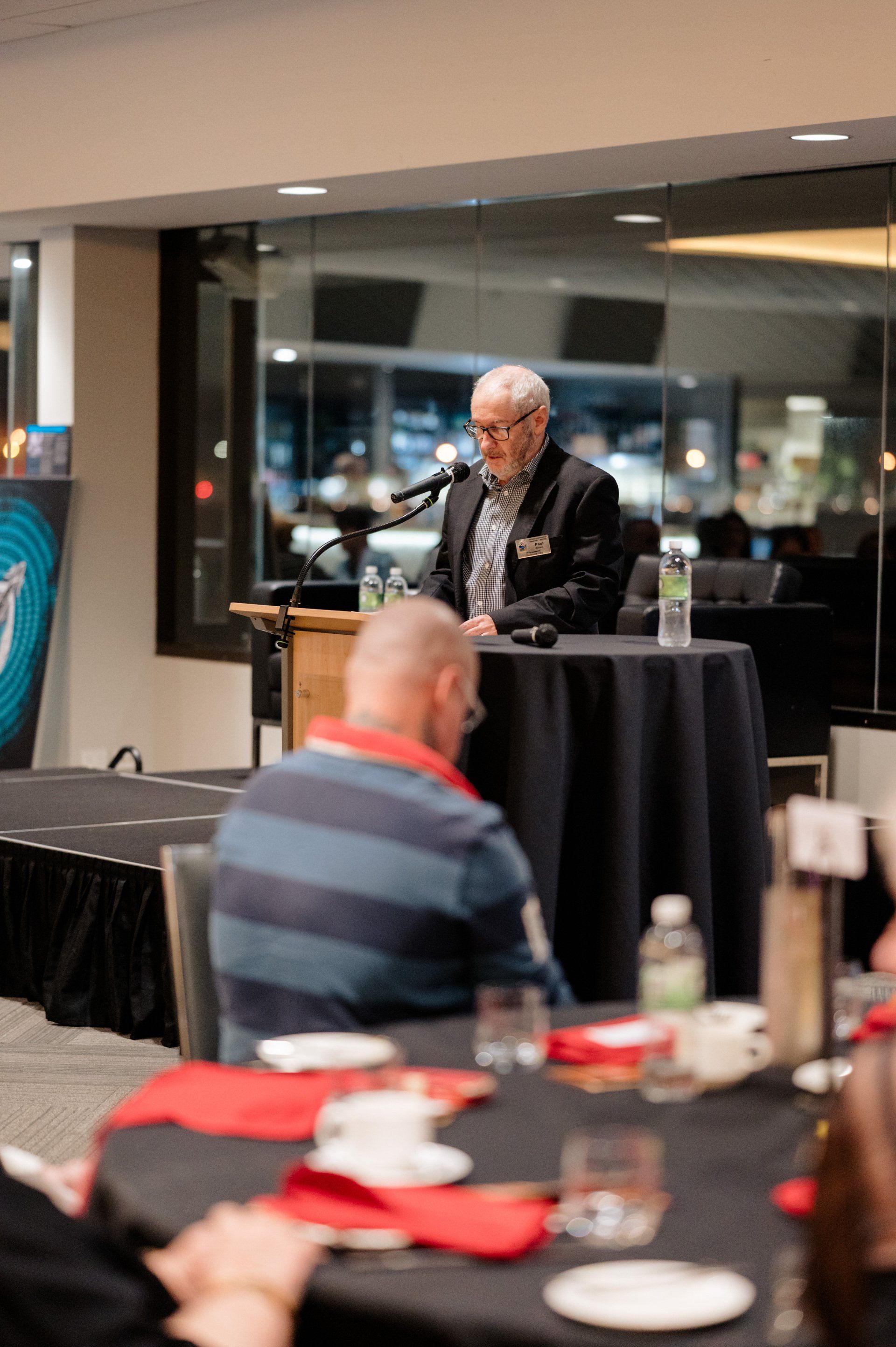 A man is standing at a podium giving a speech to a group of people sitting at tables.
