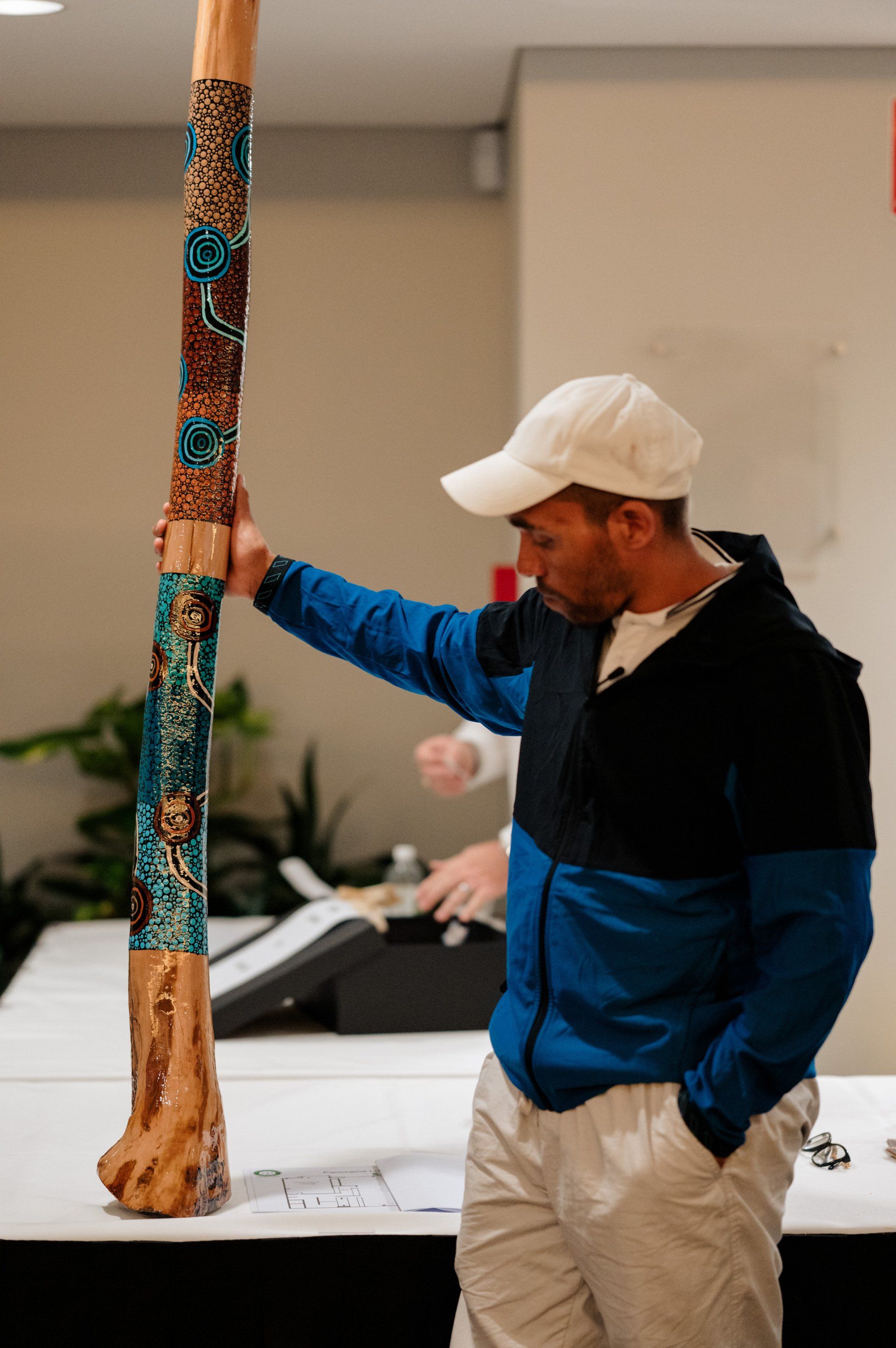 A man in a blue jacket and white hat is standing next to a tall wooden pole.