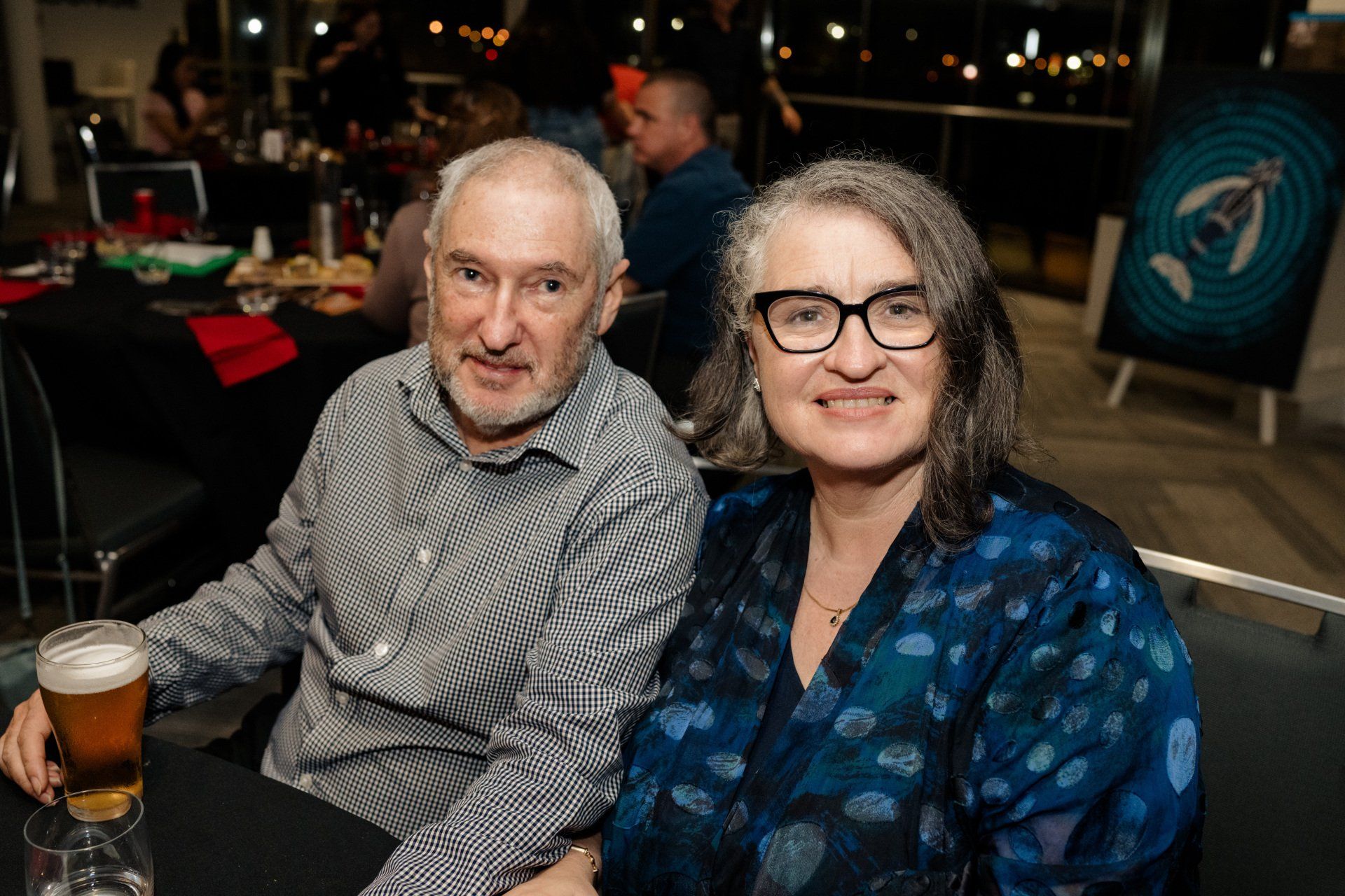 A man and a woman are sitting at a table with a glass of beer.