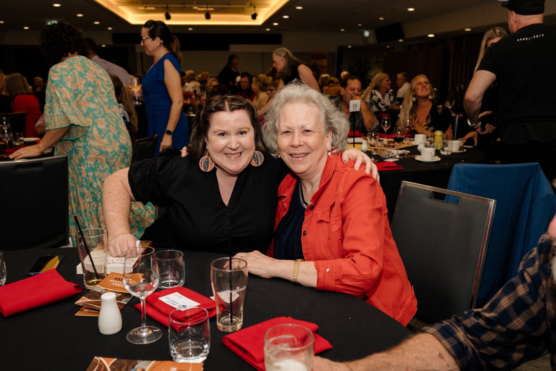 Two women are posing for a picture at a table at a party.