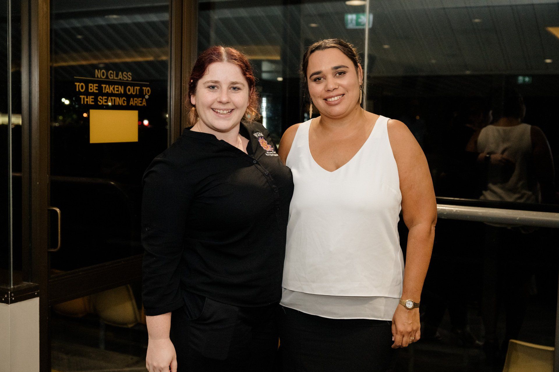 Two women are standing next to each other in front of a glass door.