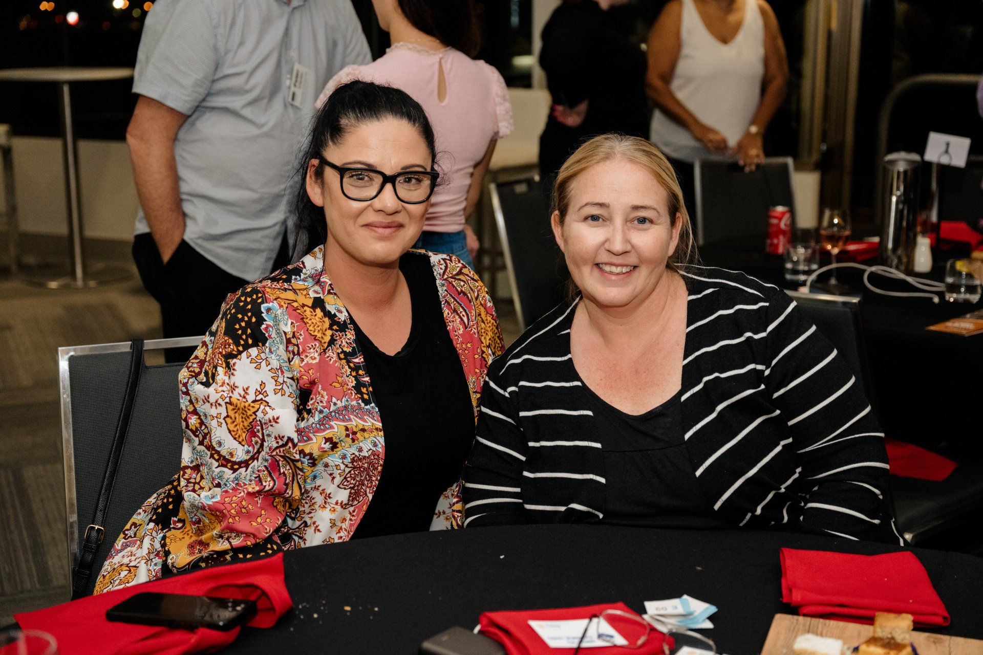 Two women are posing for a picture while sitting at a table.