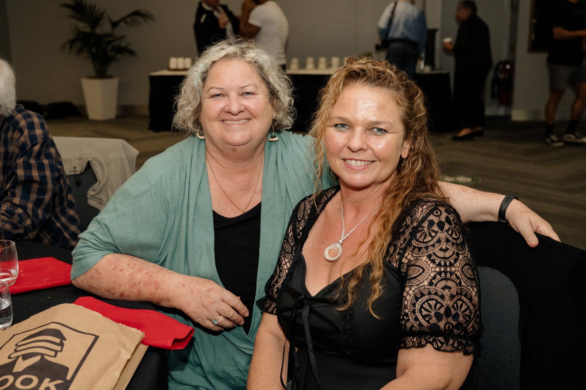 Two women are posing for a picture while sitting at a table.