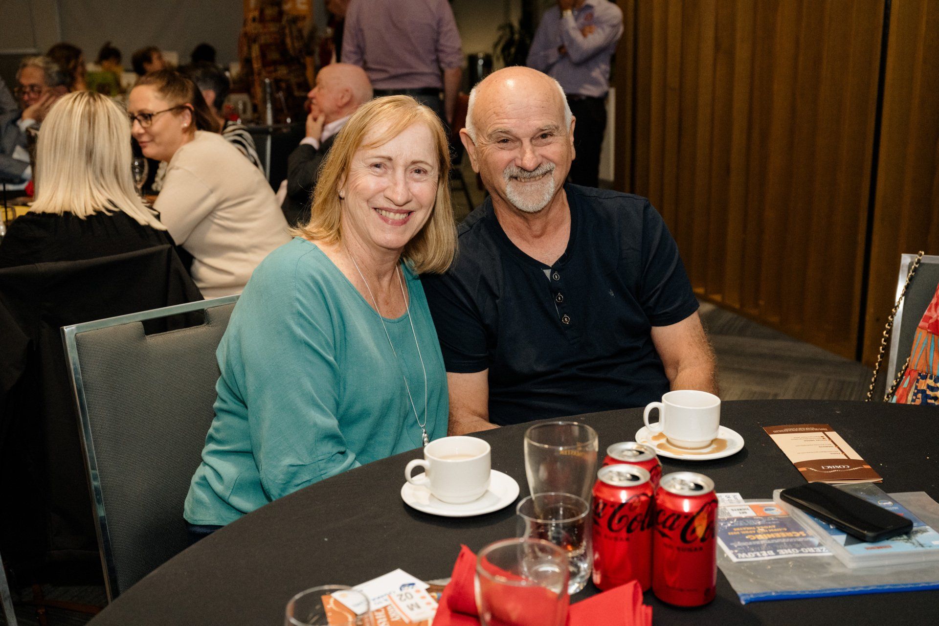 A man and a woman are sitting at a table with cups of coffee.
