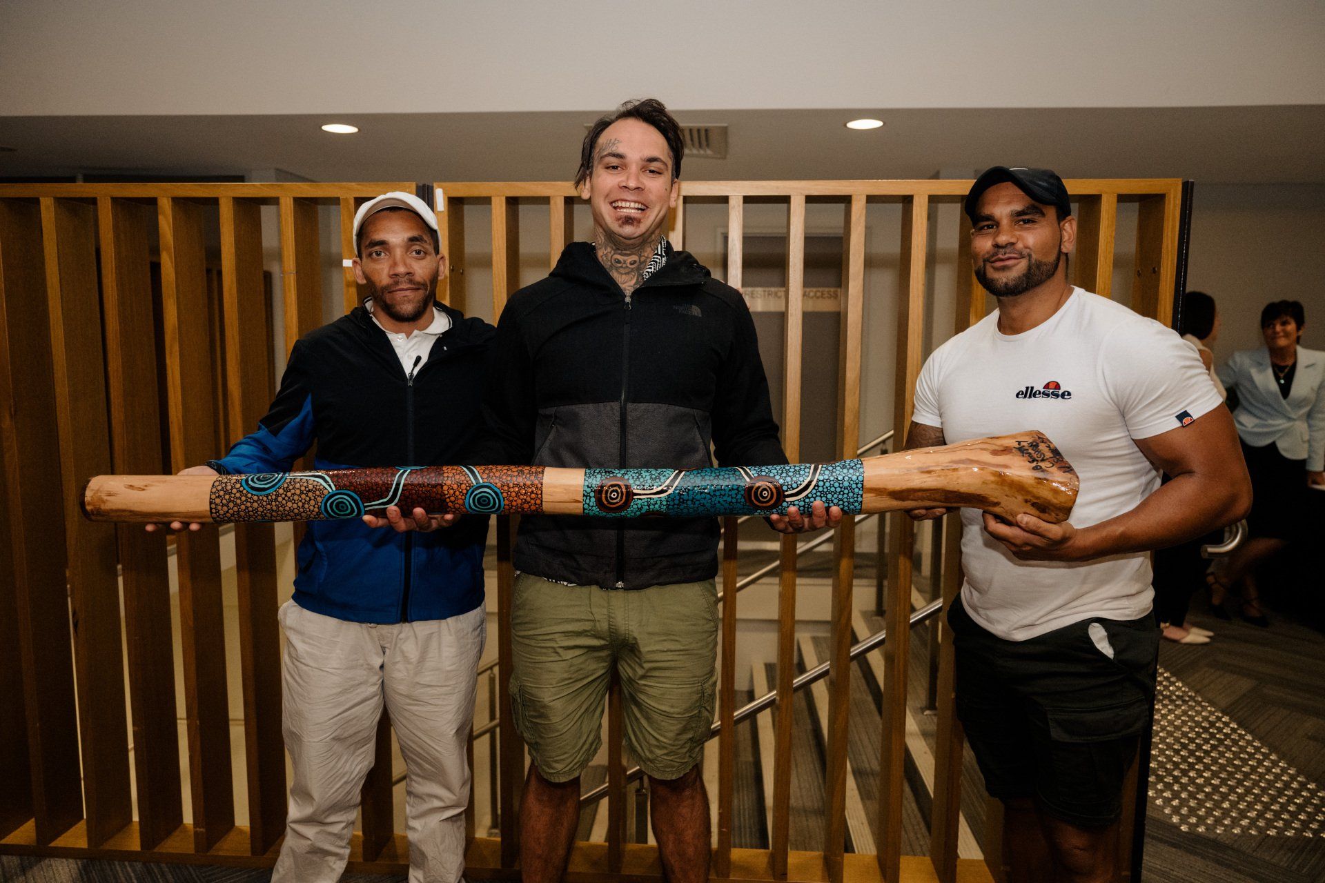 Three men are standing next to each other holding a long wooden stick.