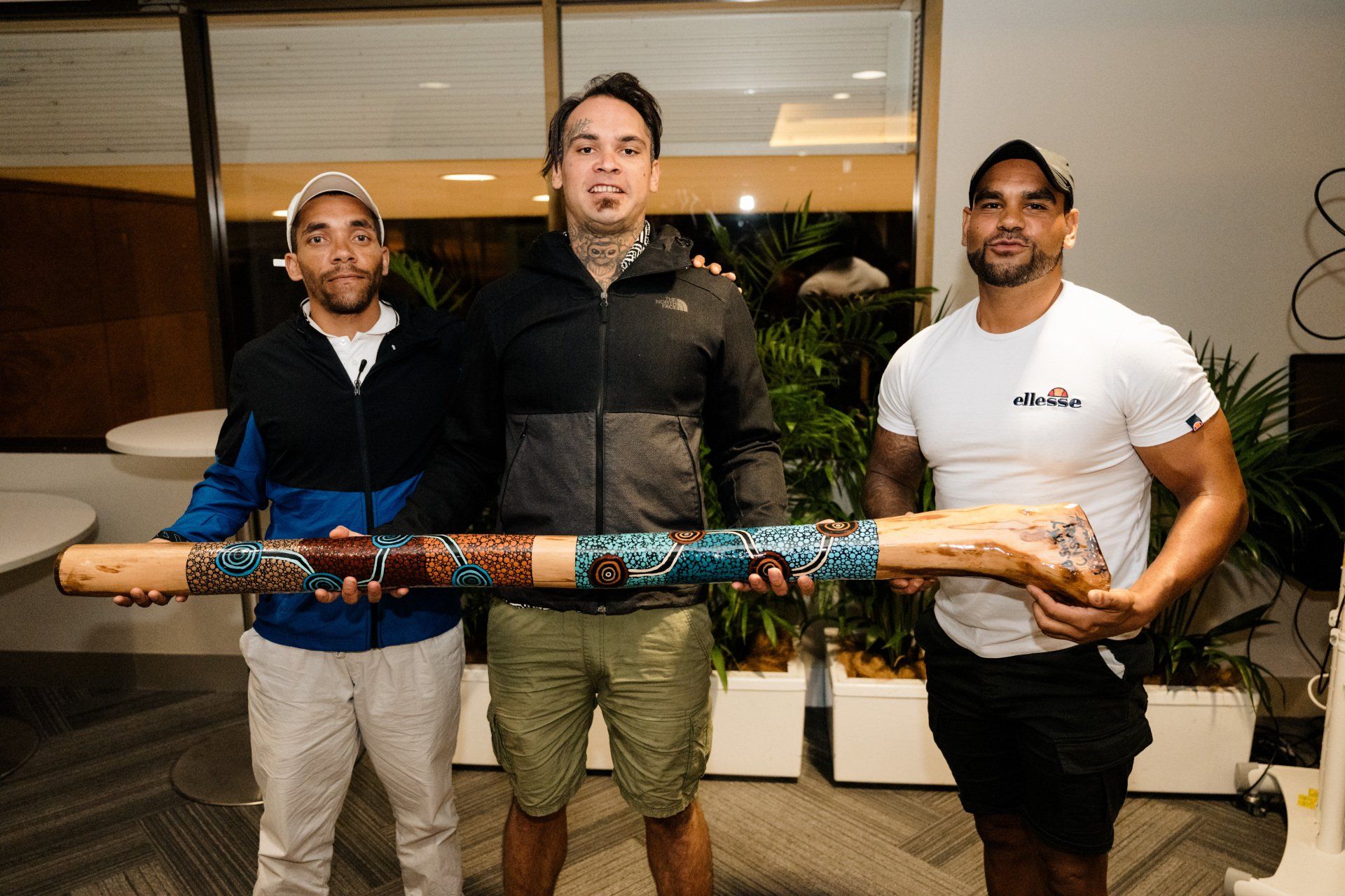 Three men are standing next to each other holding a wooden stick.