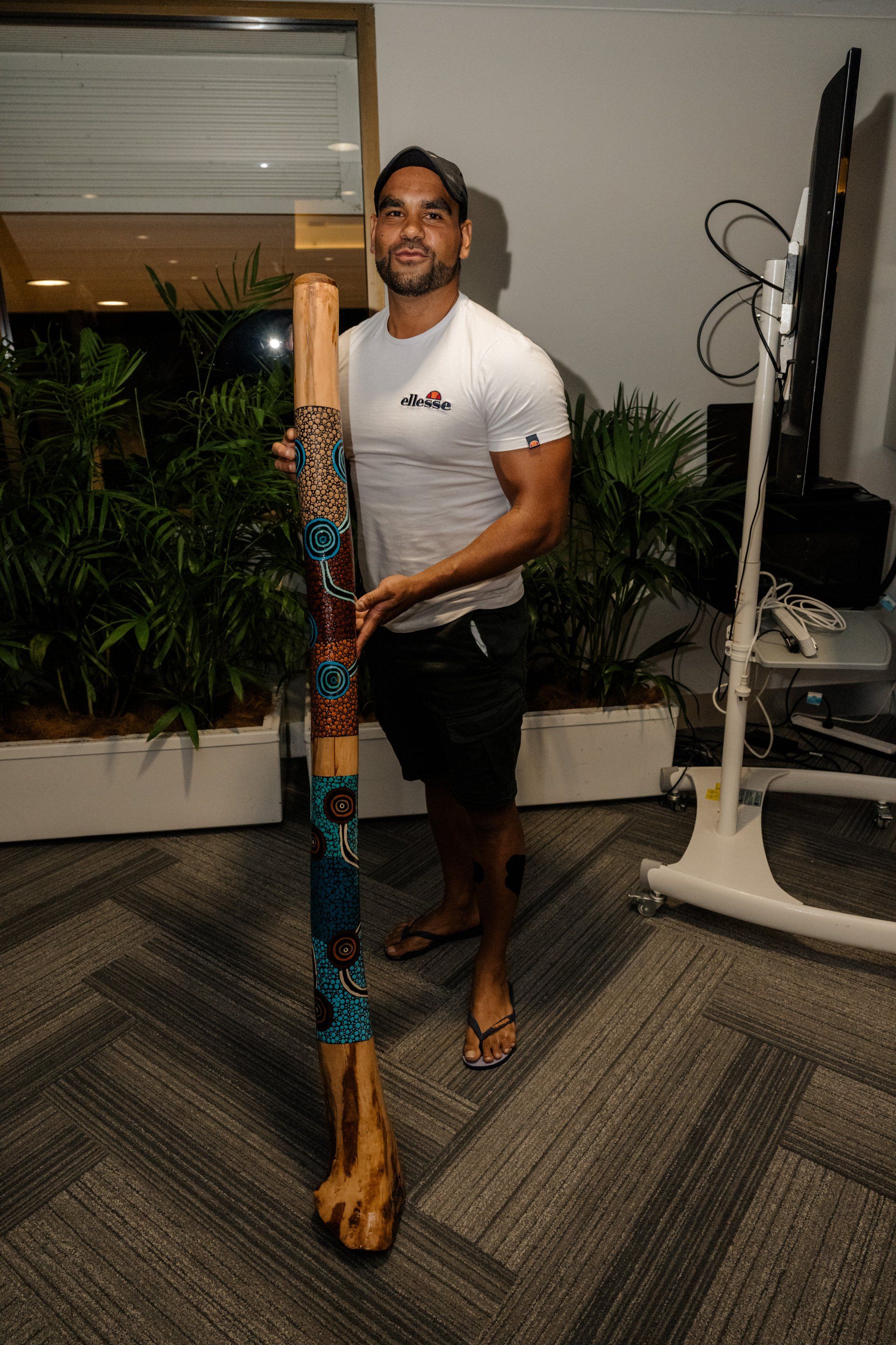 A man is holding a large wooden stick in a room.