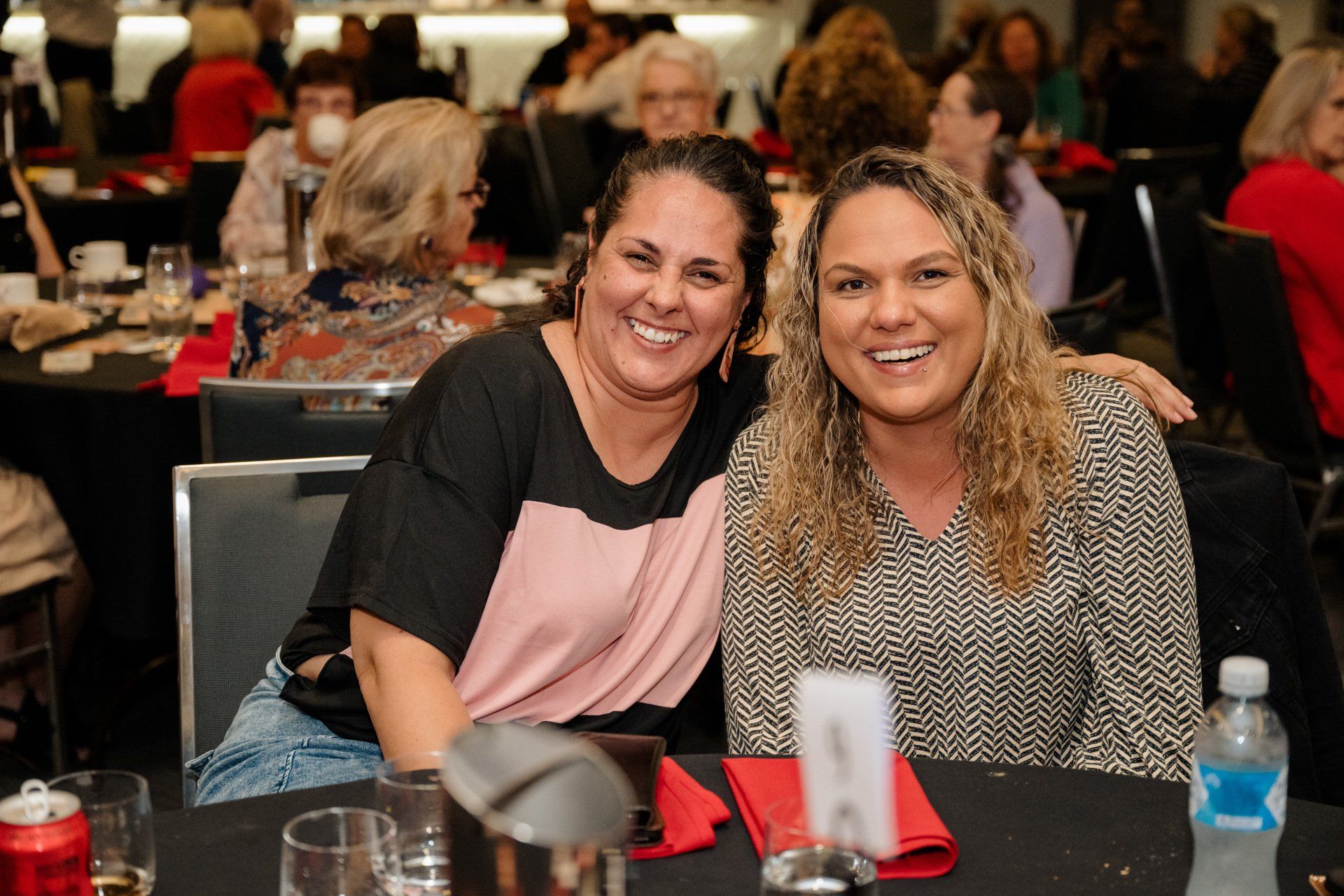 Two women are posing for a picture while sitting at a table.