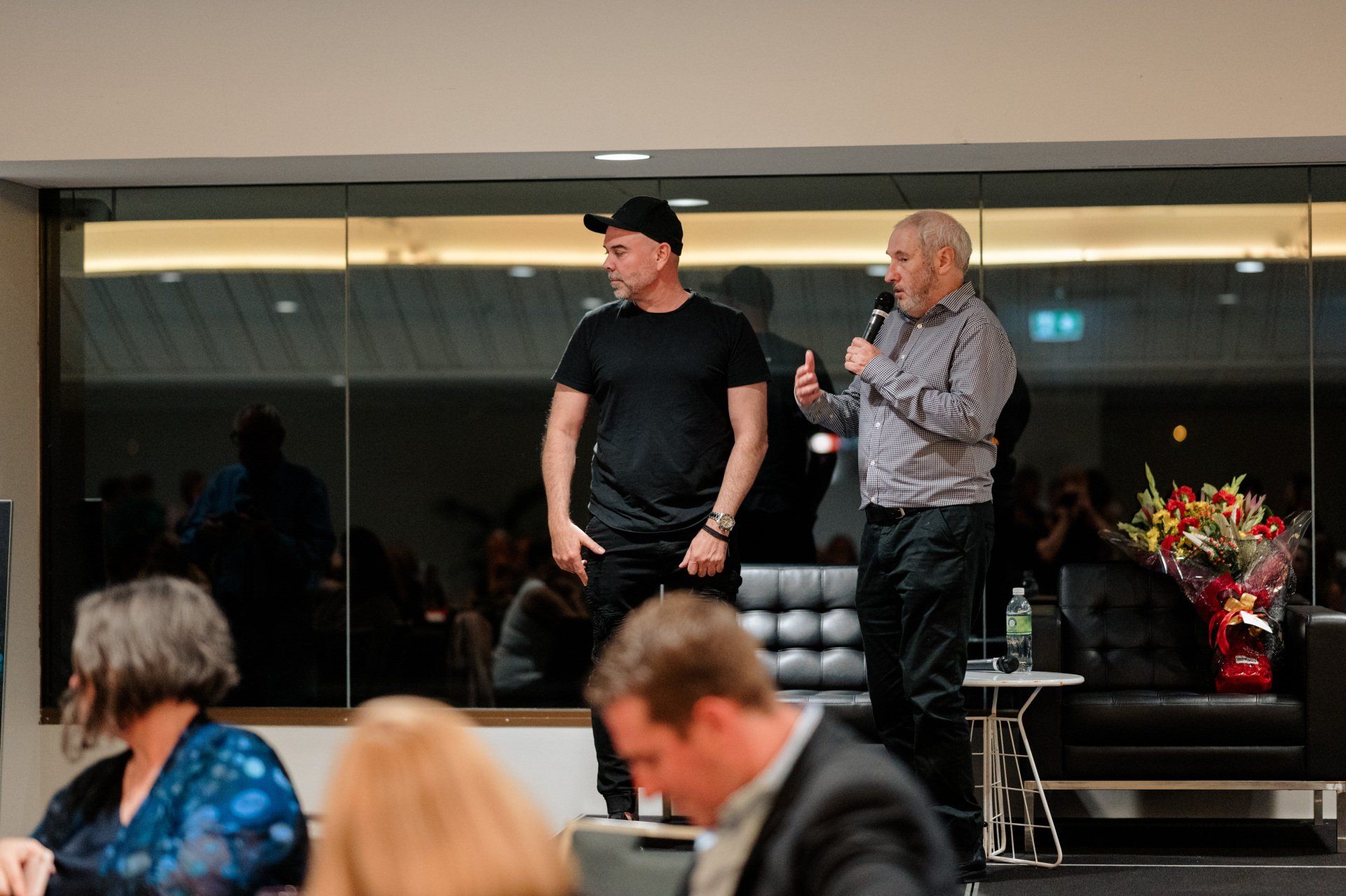 Two men are standing next to each other in a room with a microphone.