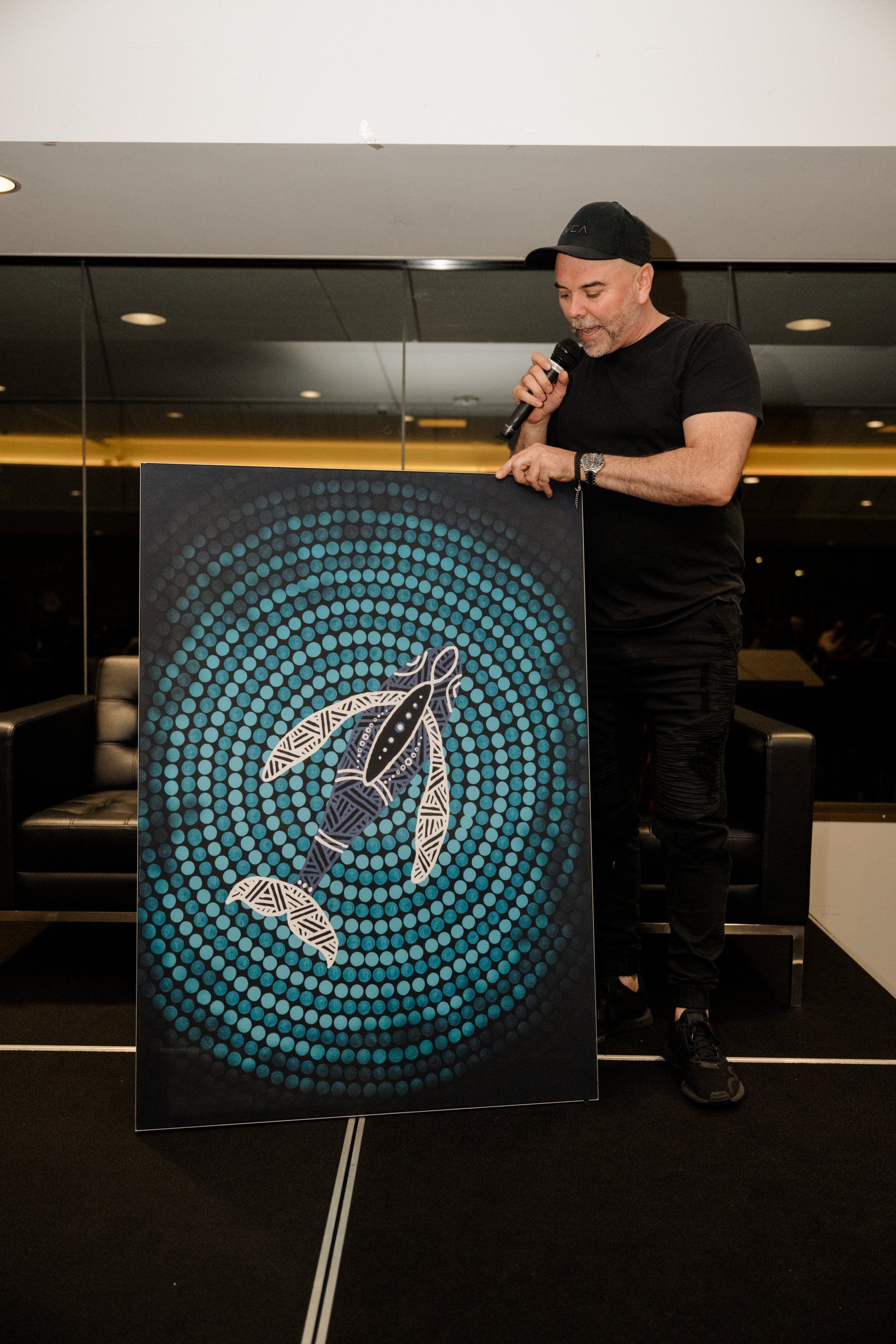 A man is holding a microphone while standing next to a painting of a sea turtle.