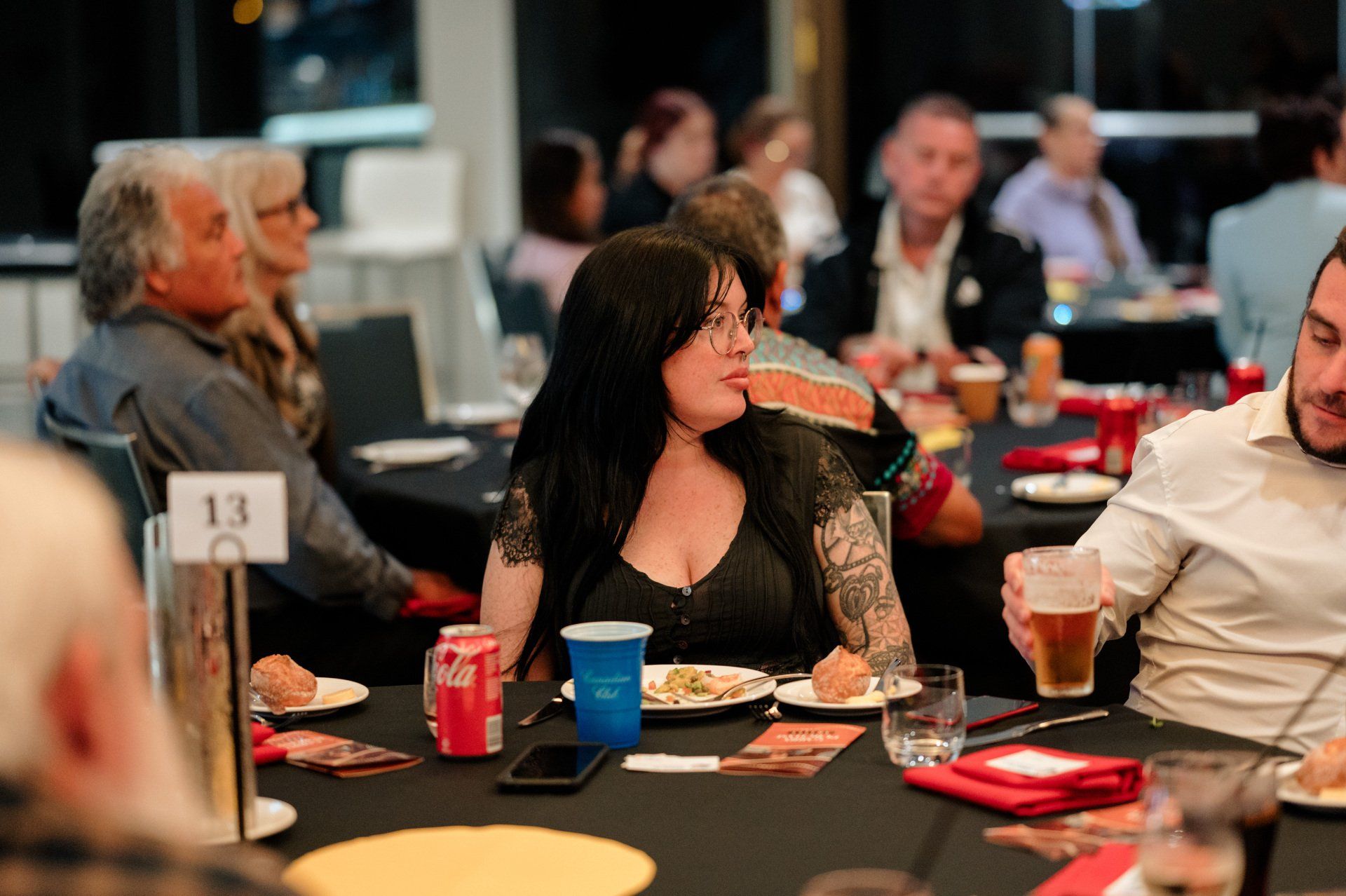 A woman is sitting at a table with plates of food and drinks.