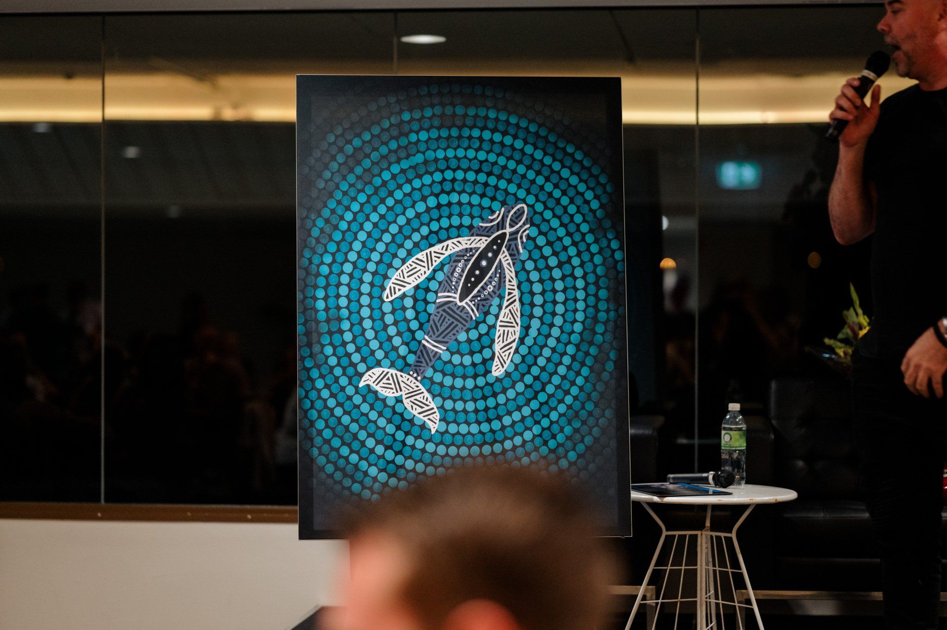A man is holding a microphone in front of a painting of a turtle.