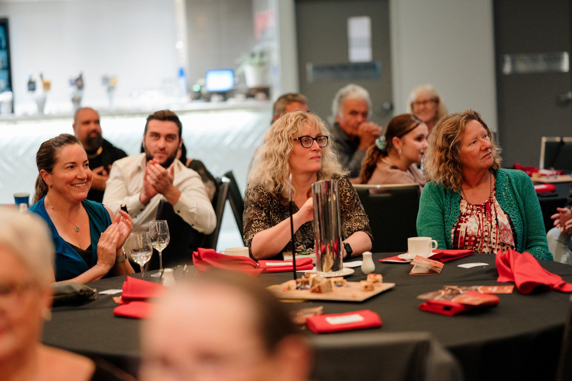 A group of people are sitting at tables in a room applauding.