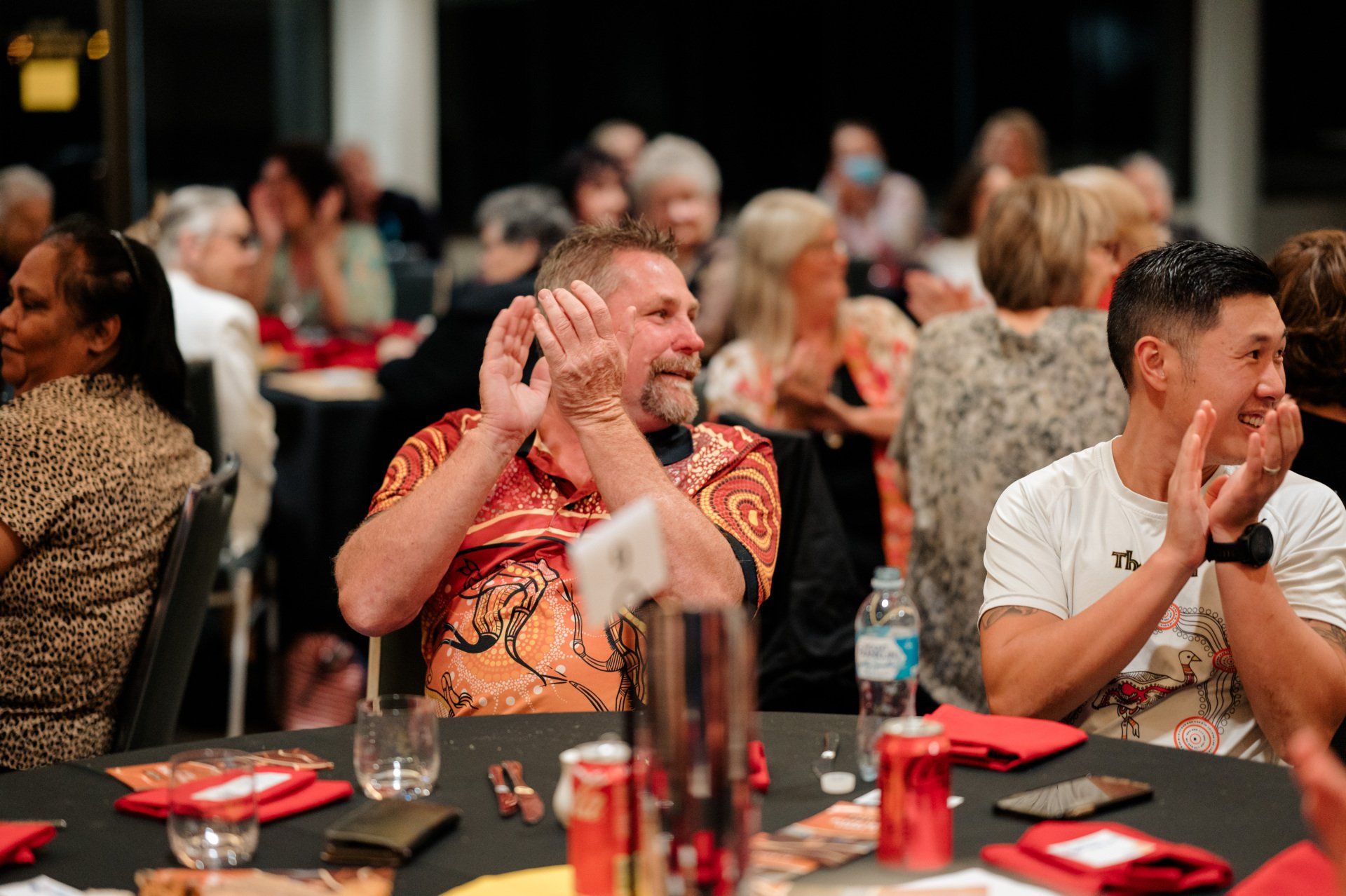 A group of people are sitting at a table clapping their hands.