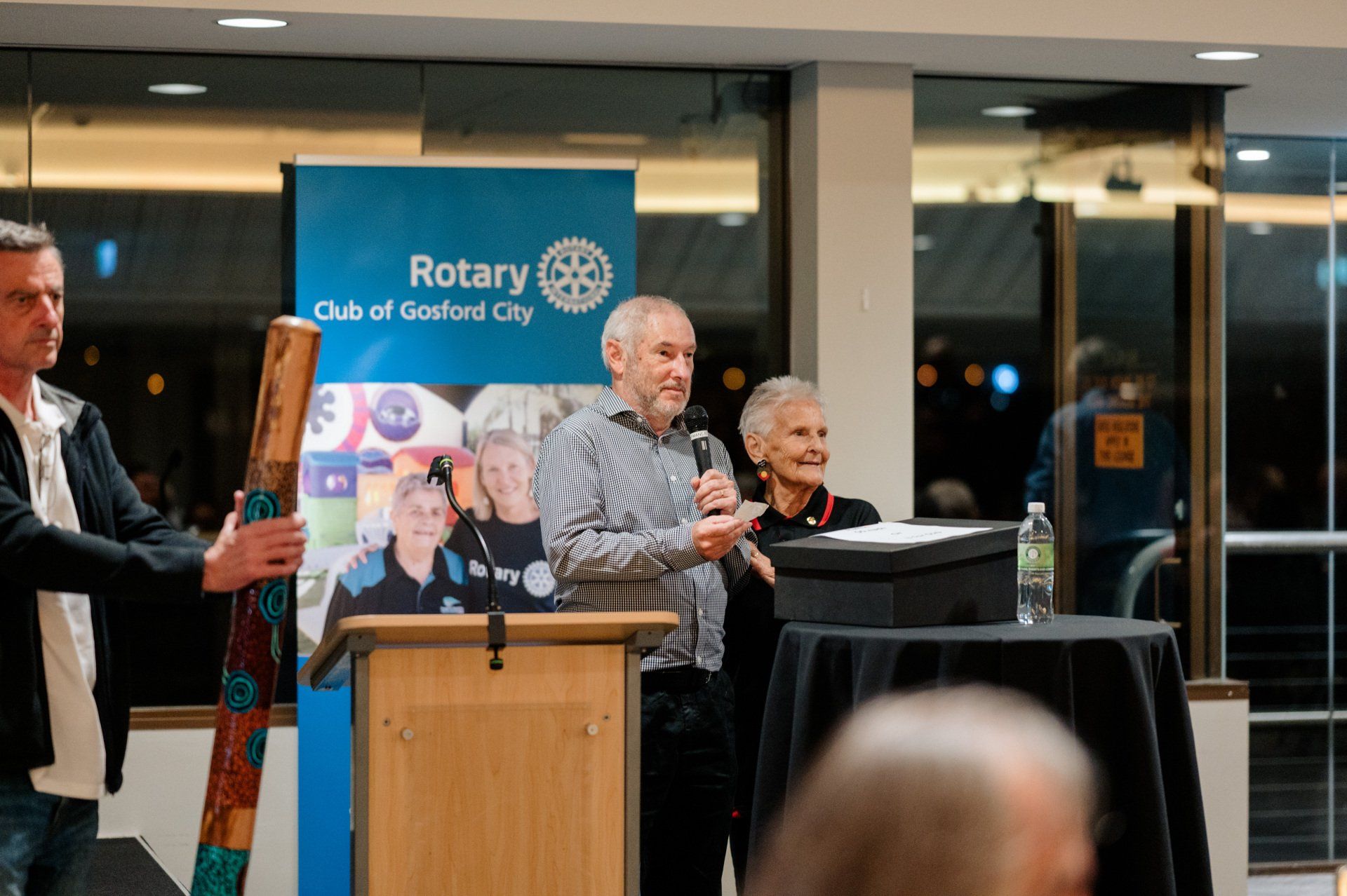 A man is standing at a podium holding a microphone in front of a group of people.