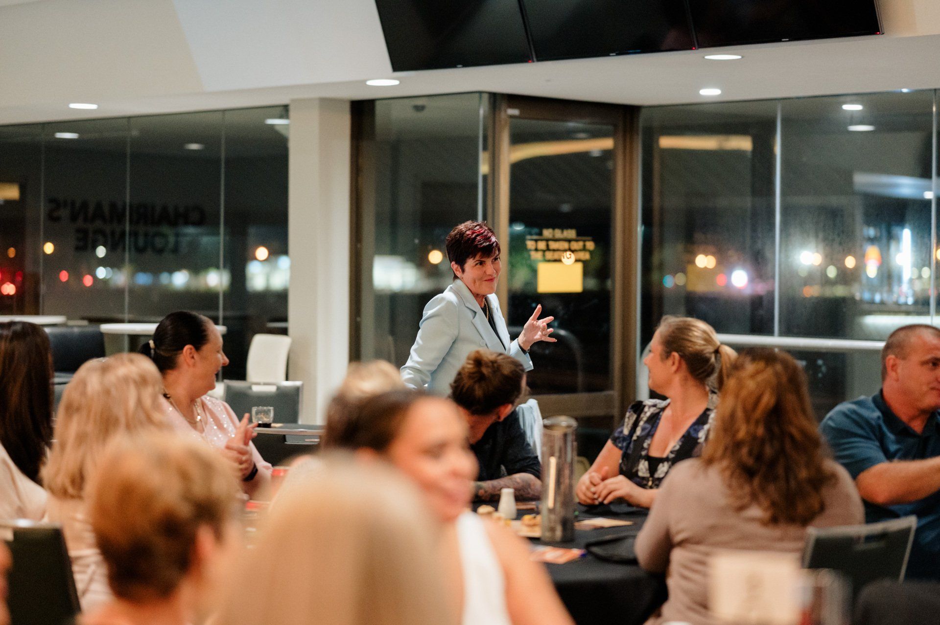 A woman is giving a presentation to a group of people sitting at tables.