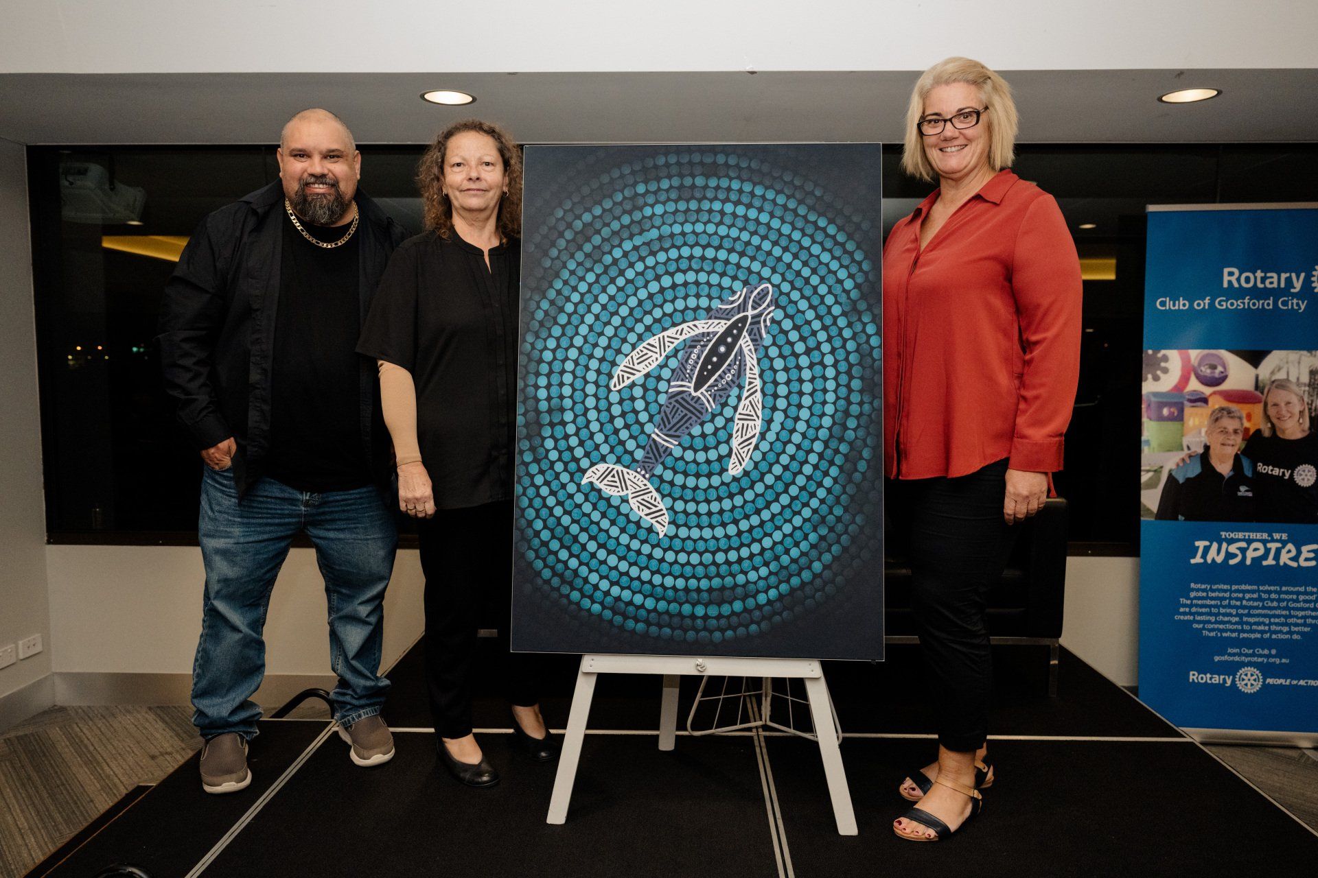 A group of people standing next to a painting on an easel.