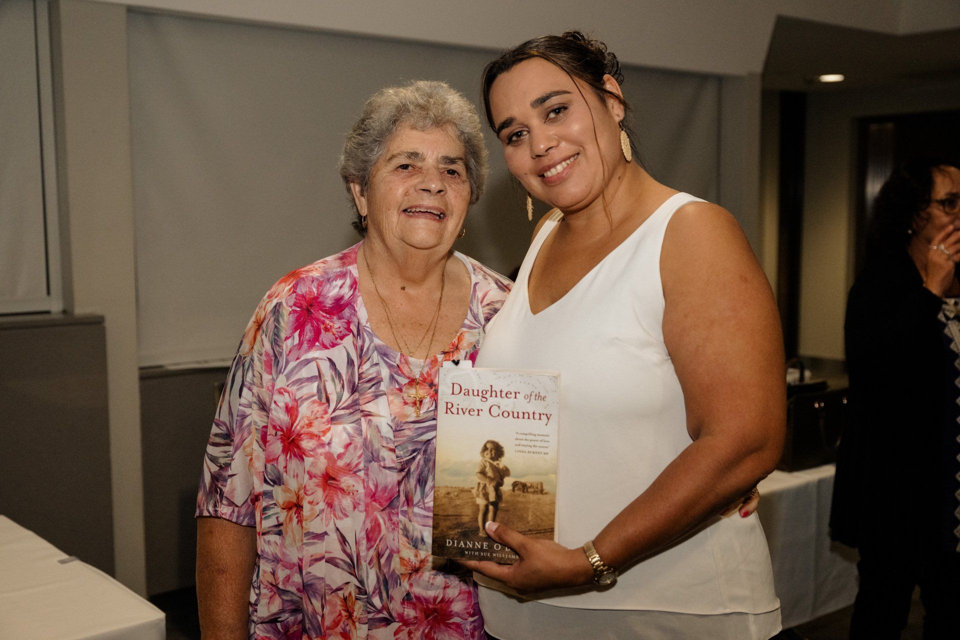 Two women are standing next to each other holding a book.