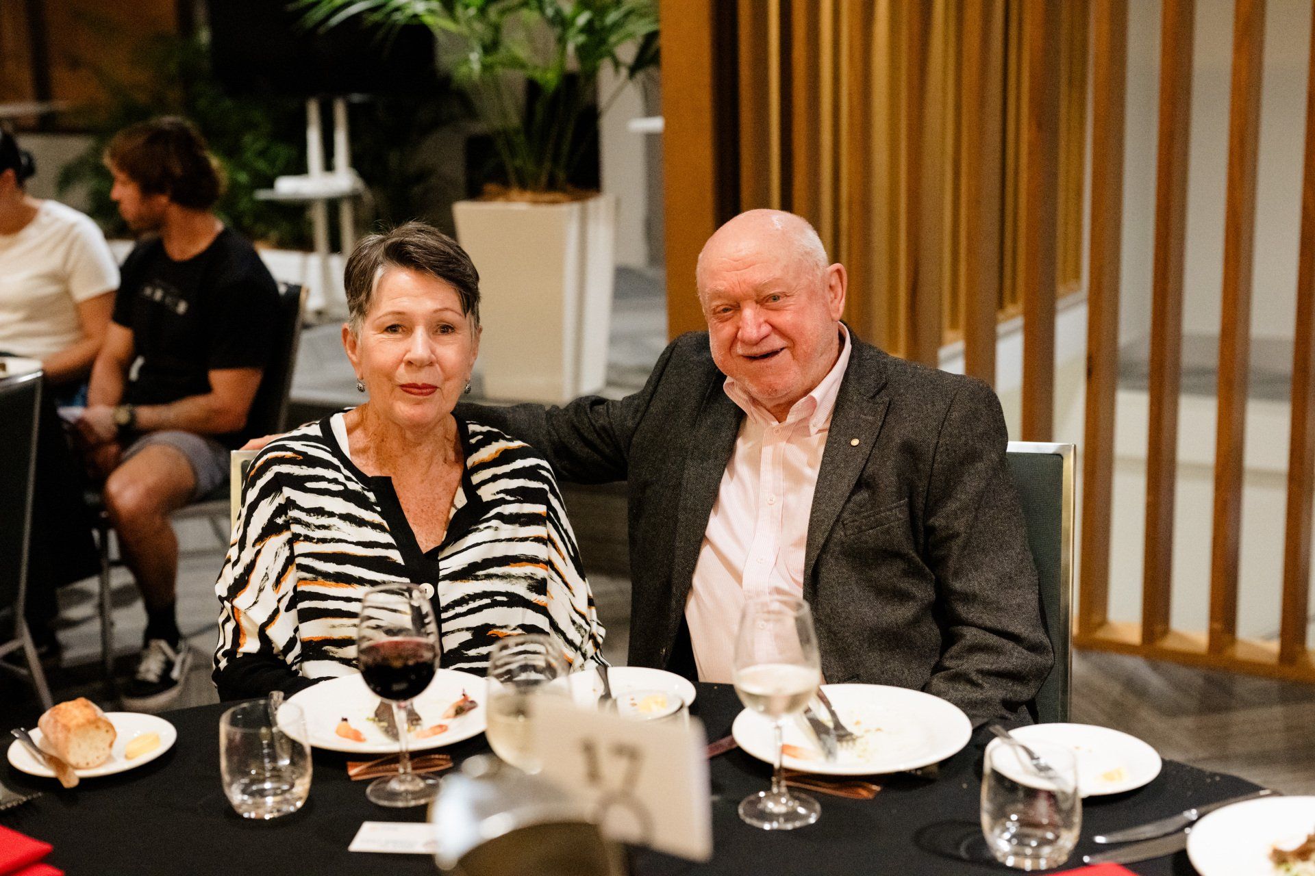 A man and a woman are sitting at a table with plates and glasses of wine.