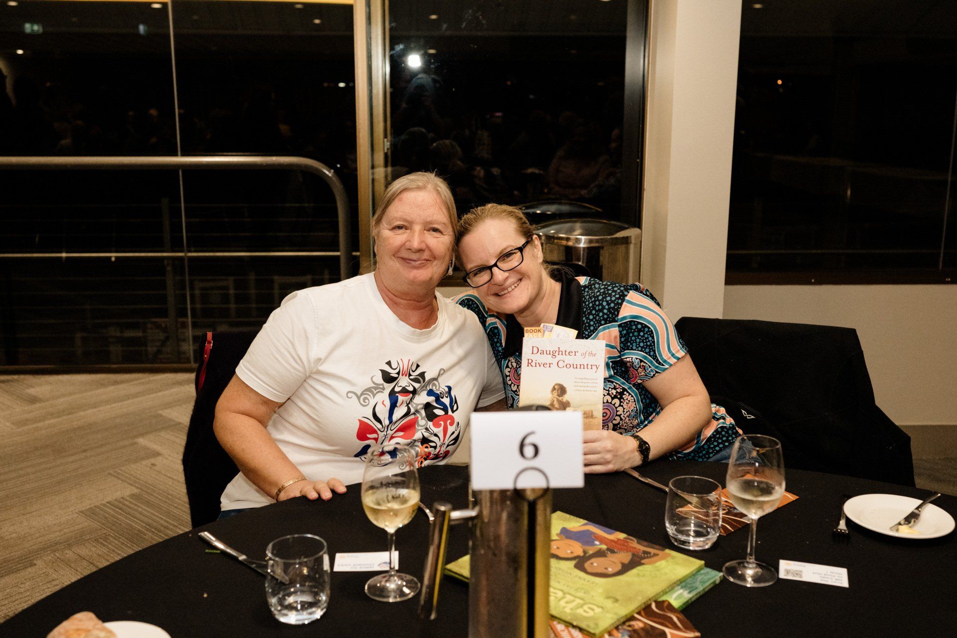 Two women are sitting at a table with glasses of wine.